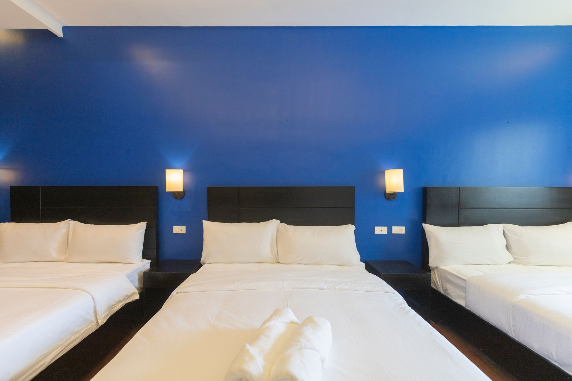 Three beds in a hotel room with a vibrant blue wall and warm lighting.