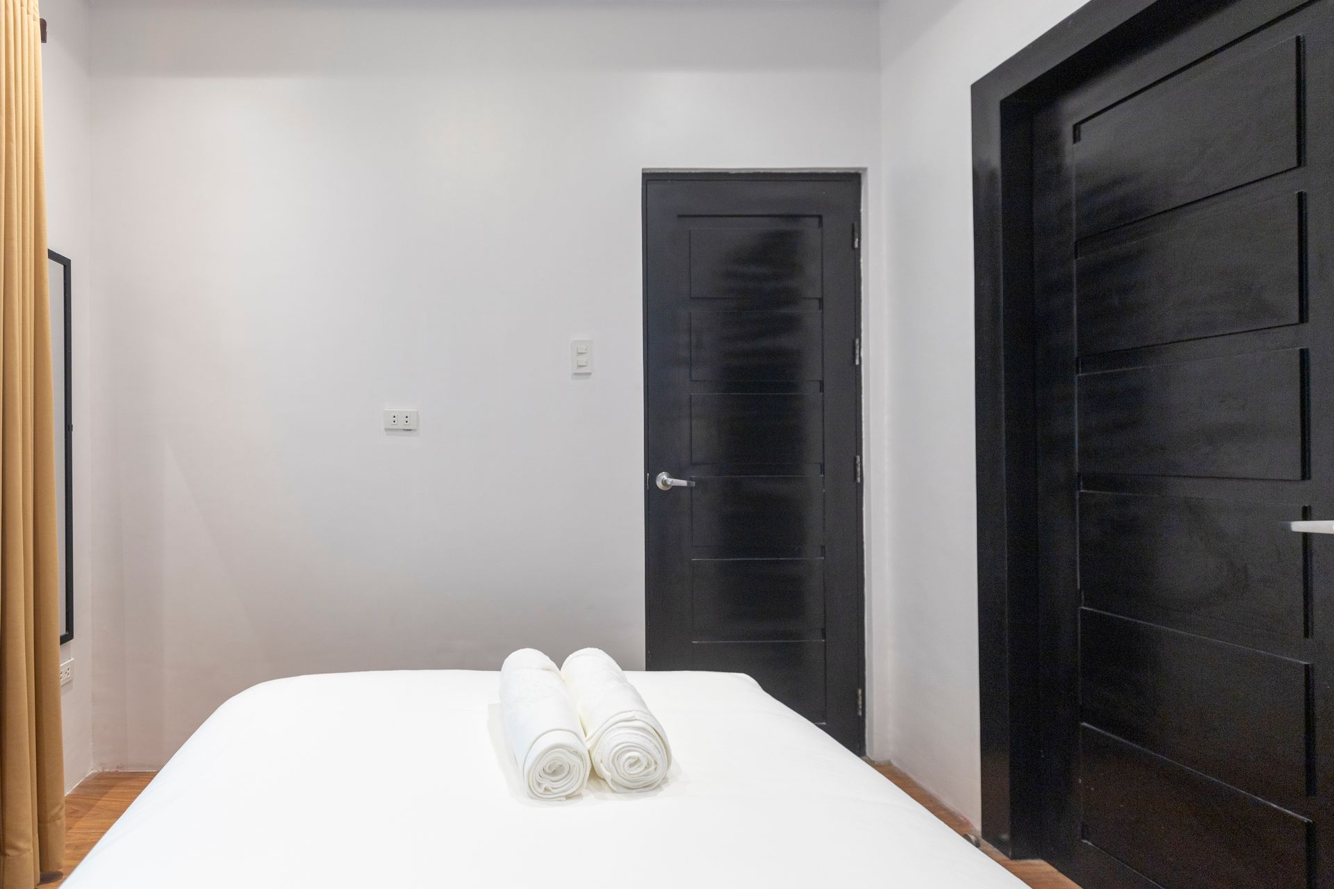 White bed with rolled towels, facing black doors on either side.