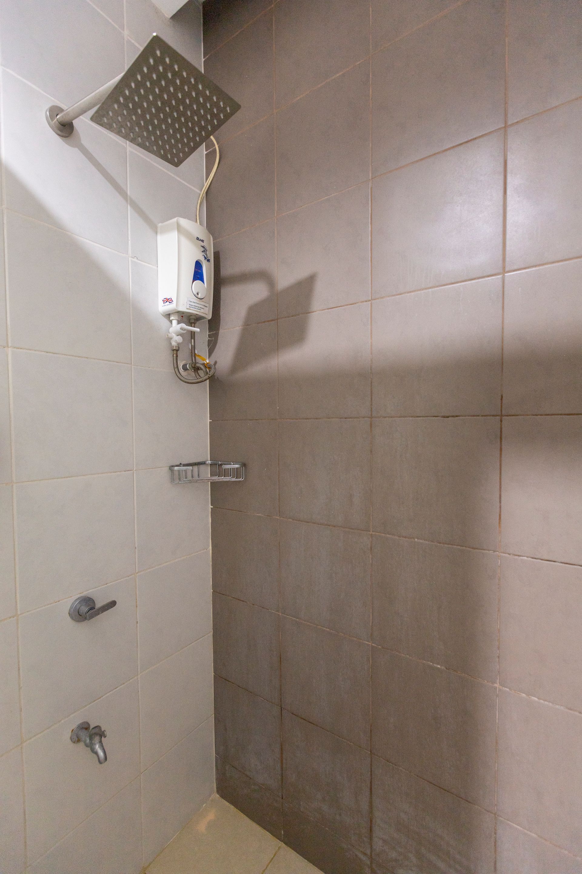 Shower with square rain showerhead, wall-mounted water heater, and soap holder on tiled walls.
