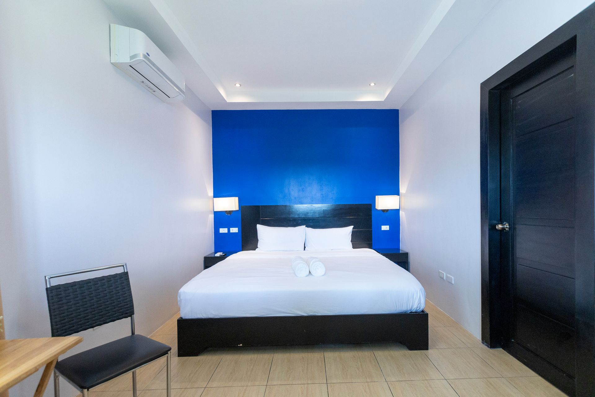 Bedroom with bed against a blue wall, chair, black door, and air conditioner.