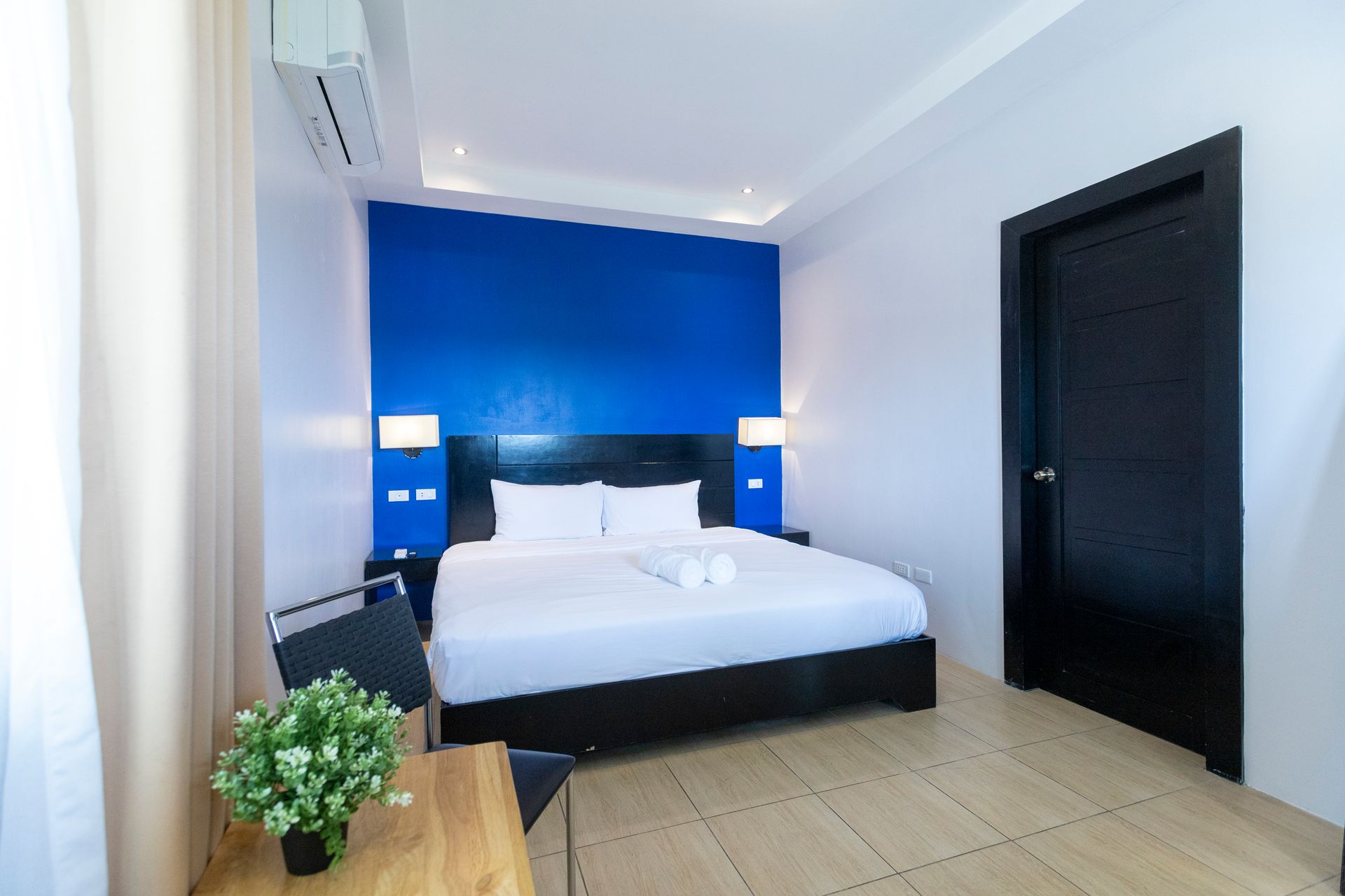 Bedroom with a blue accent wall, white bedding, black door and furniture, and a small plant.