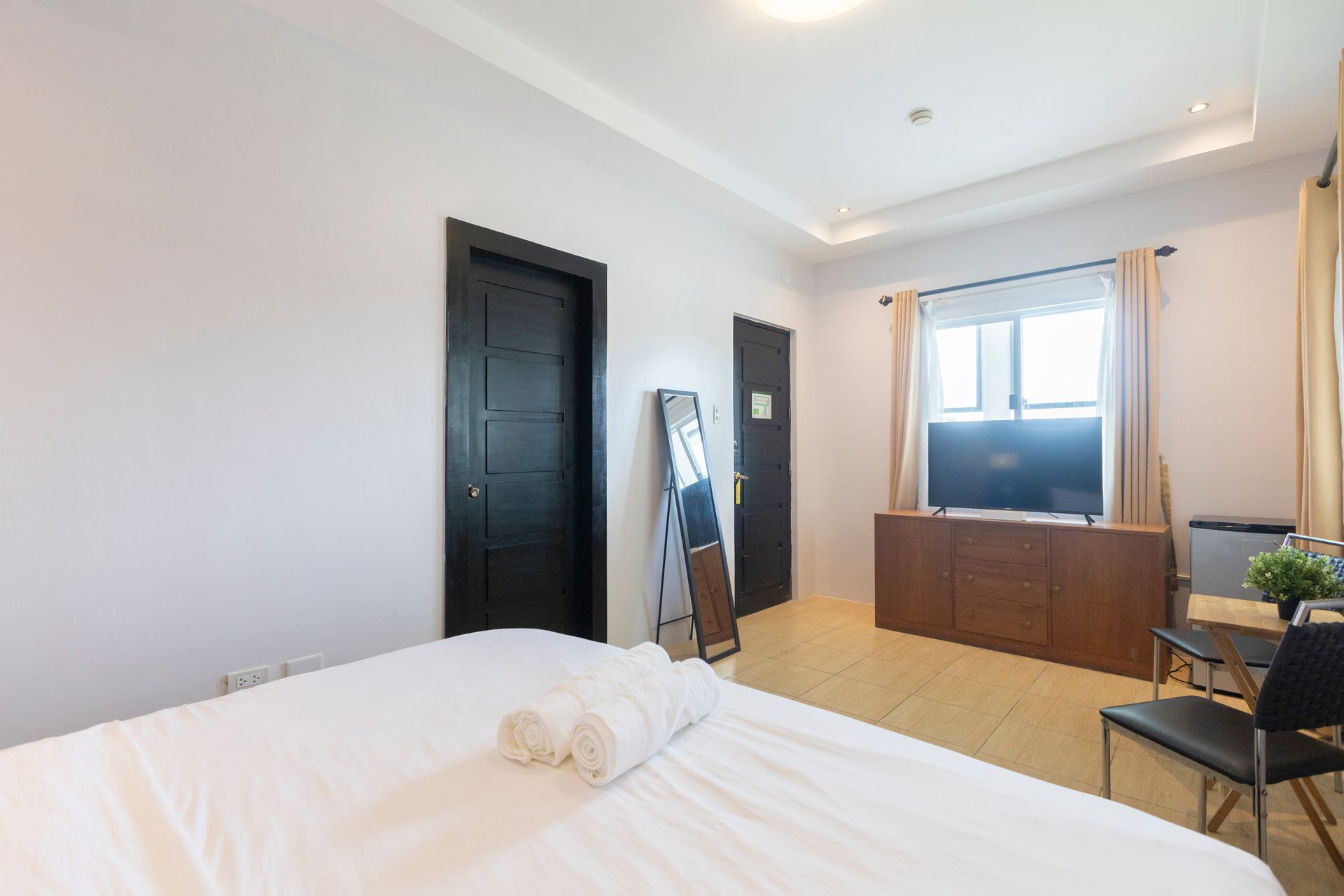 Bedroom with a bed, TV, two black doors, a mirror, and a window.