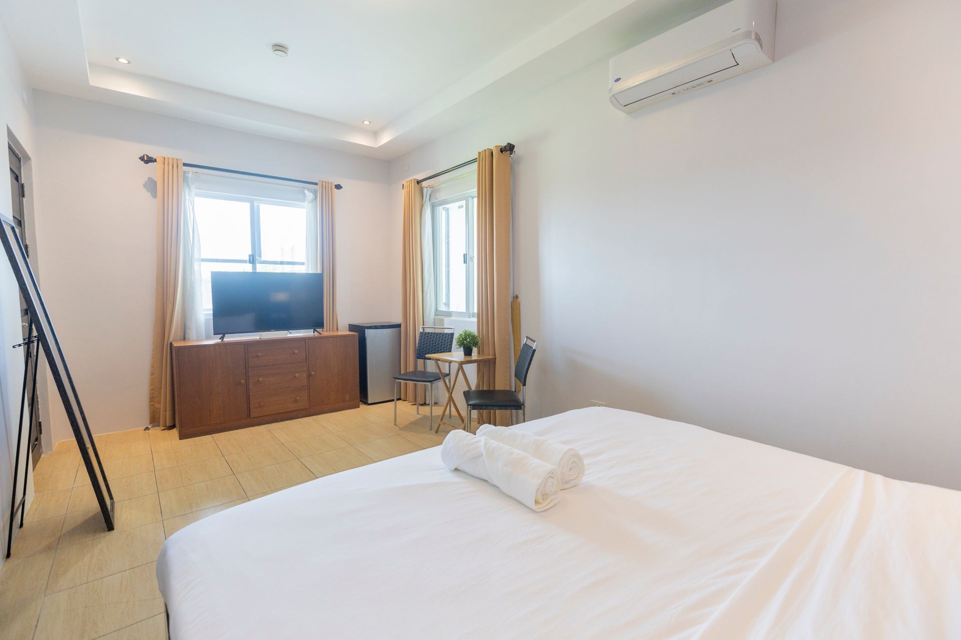 Bedroom with white walls, bed, TV, small table, and air conditioner.