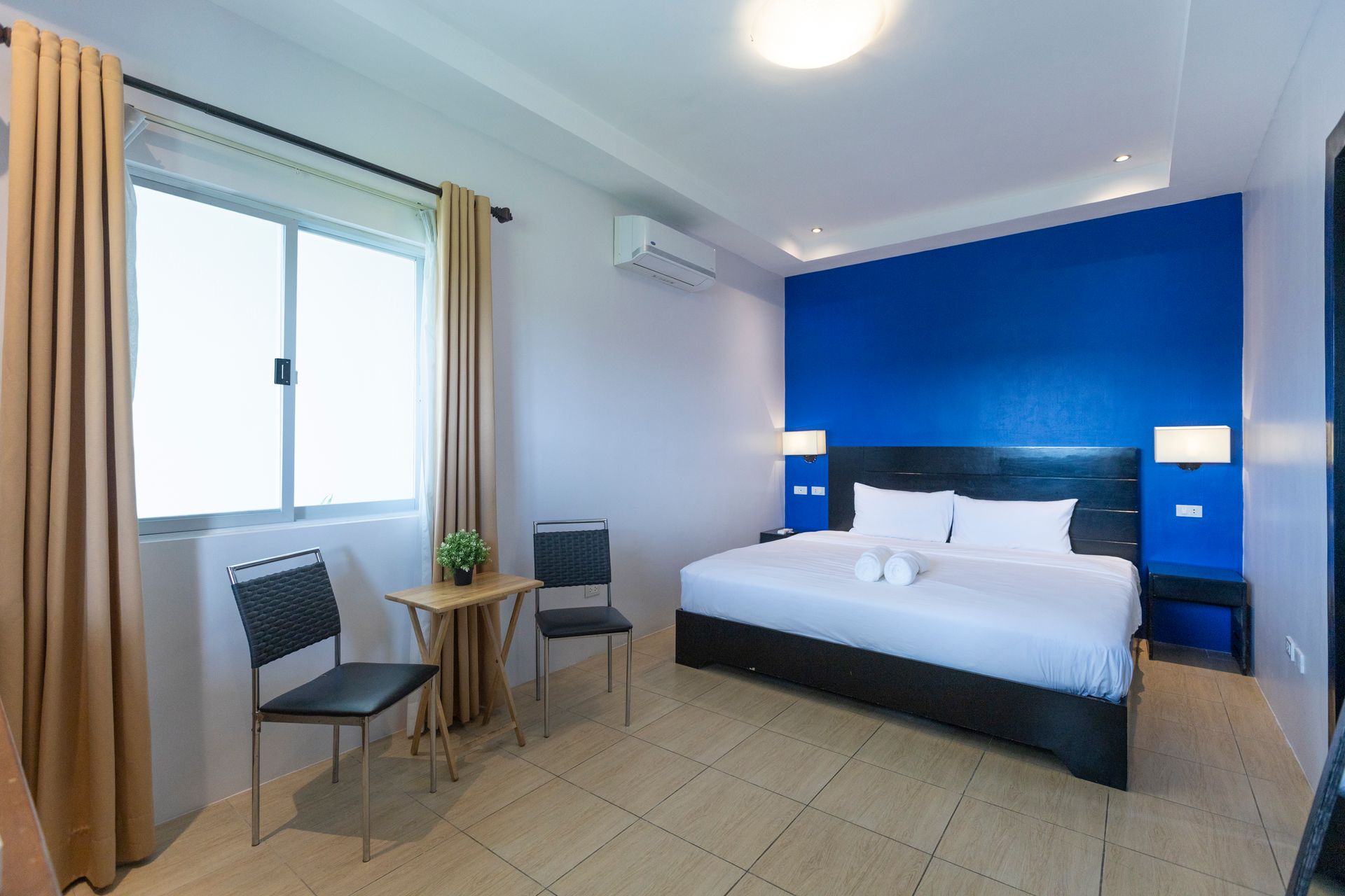 Hotel room with king bed, blue accent wall, window with curtains, and seating area.