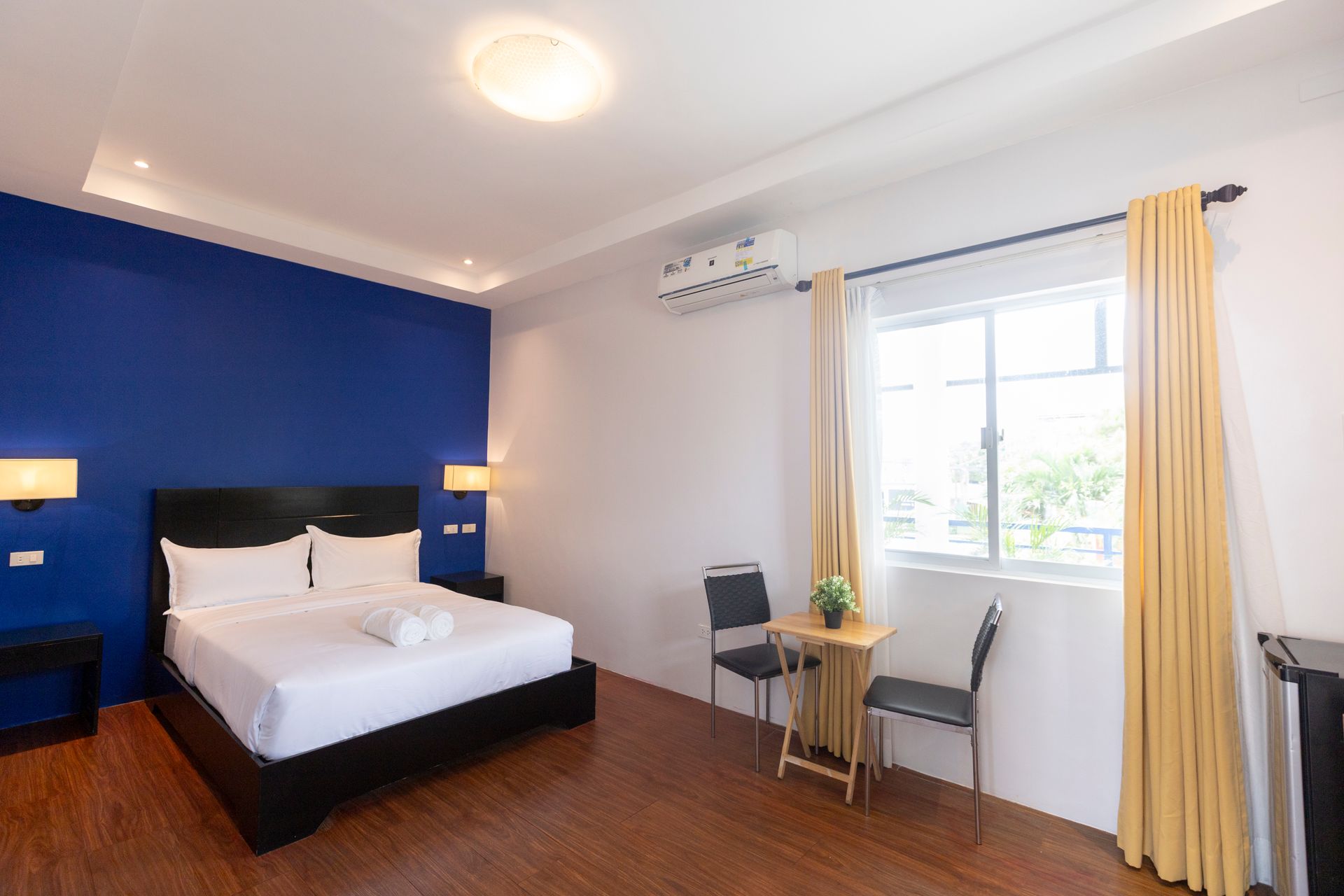 Hotel room with a blue accent wall, double bed, and small table by the window.