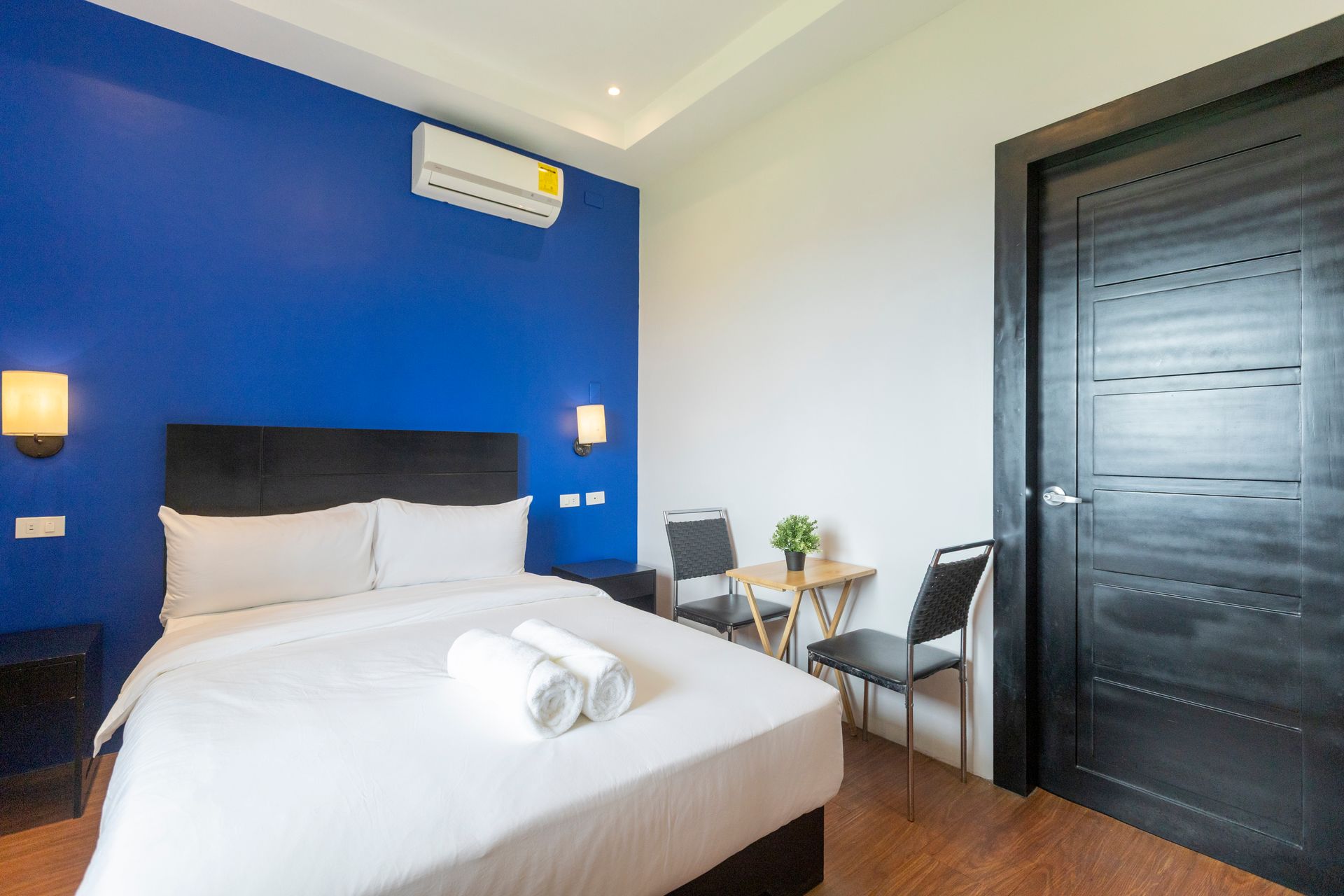 Bedroom with blue accent wall, double bed, small table with chairs, and a black door.