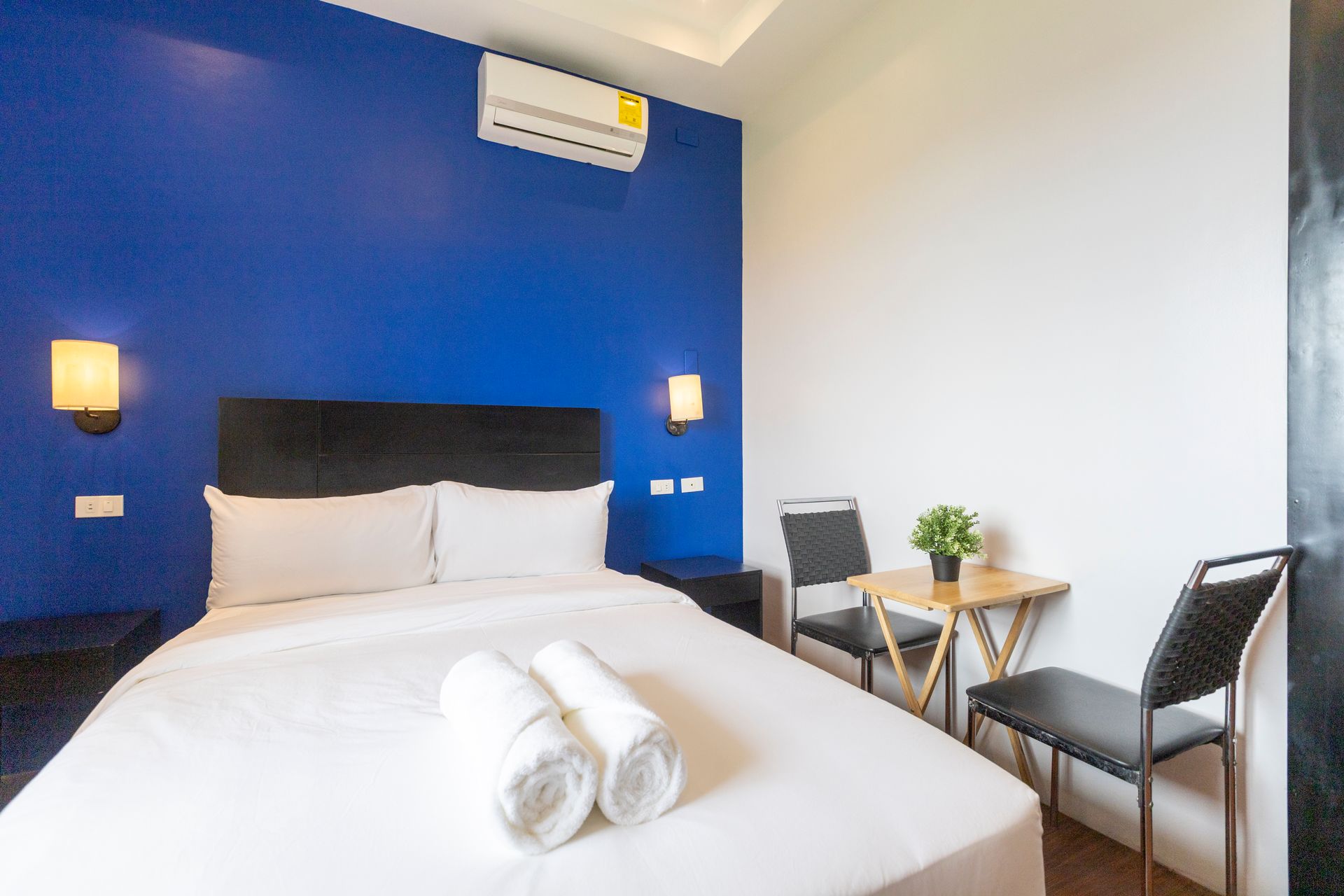 Bedroom with a blue accent wall, white bedding, table, chairs, and air conditioner.