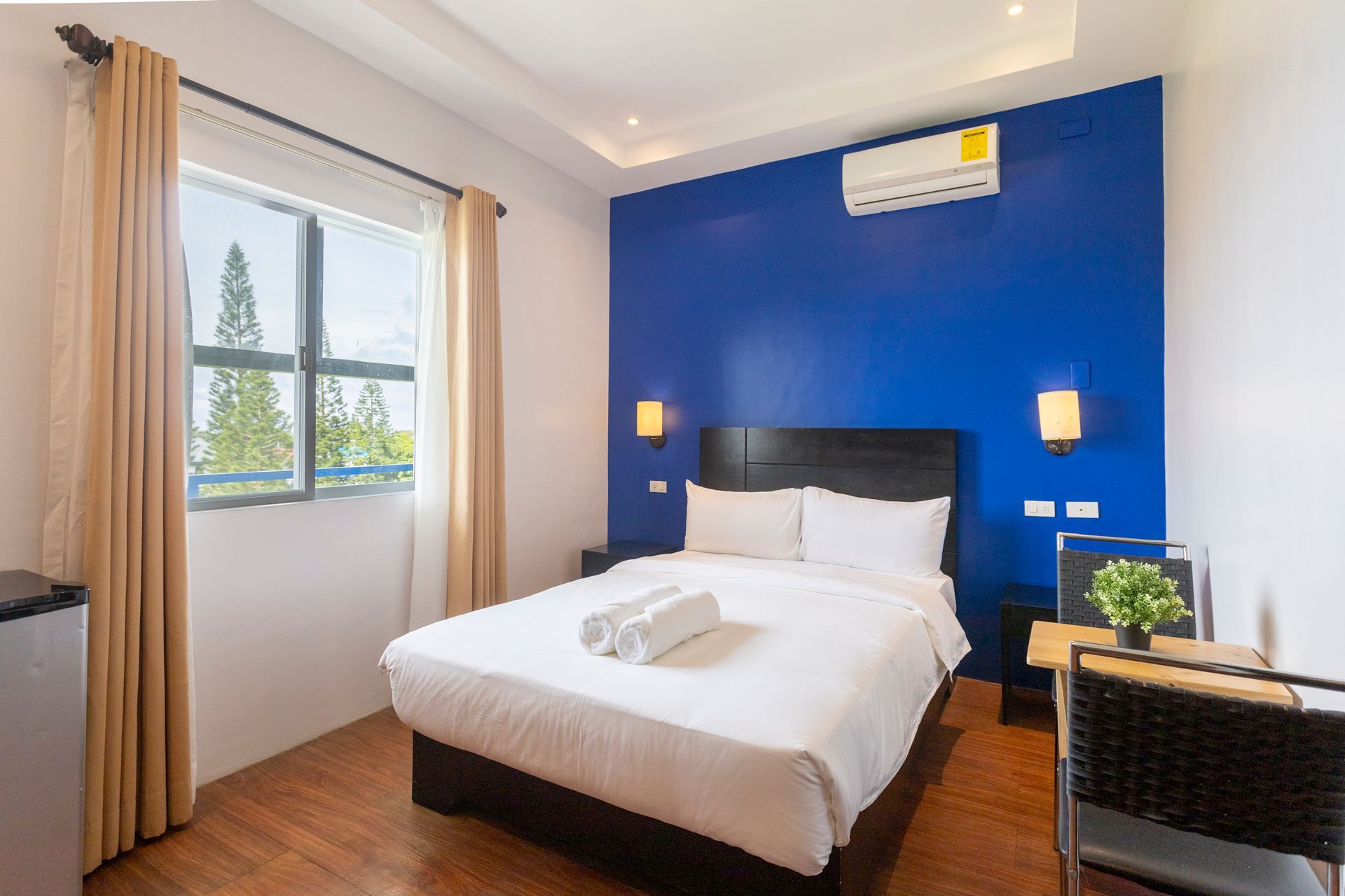Hotel room with a blue accent wall, double bed, window, and small desk.