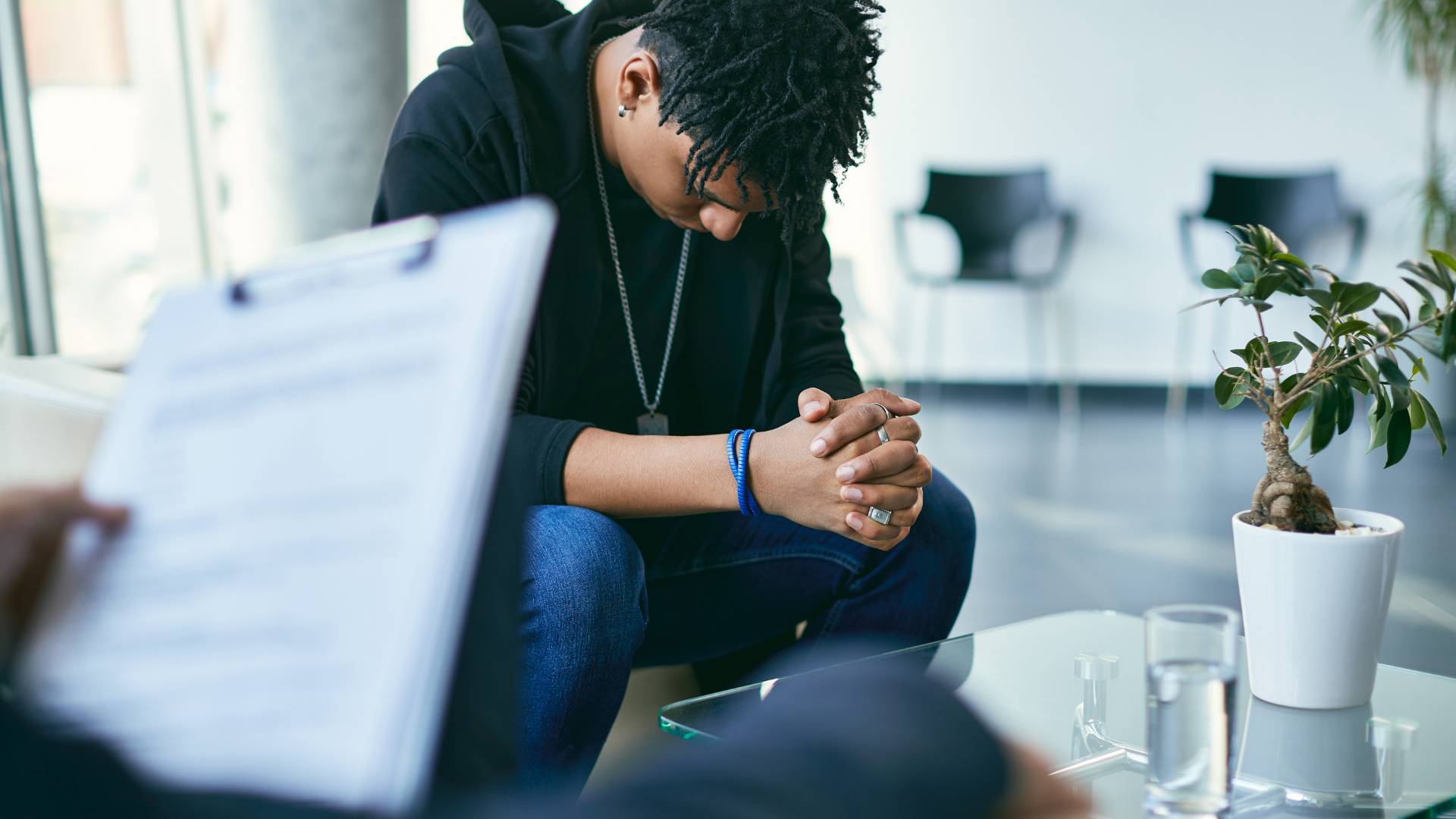 A young man is sitting on a couch with his hands folded in prayer.