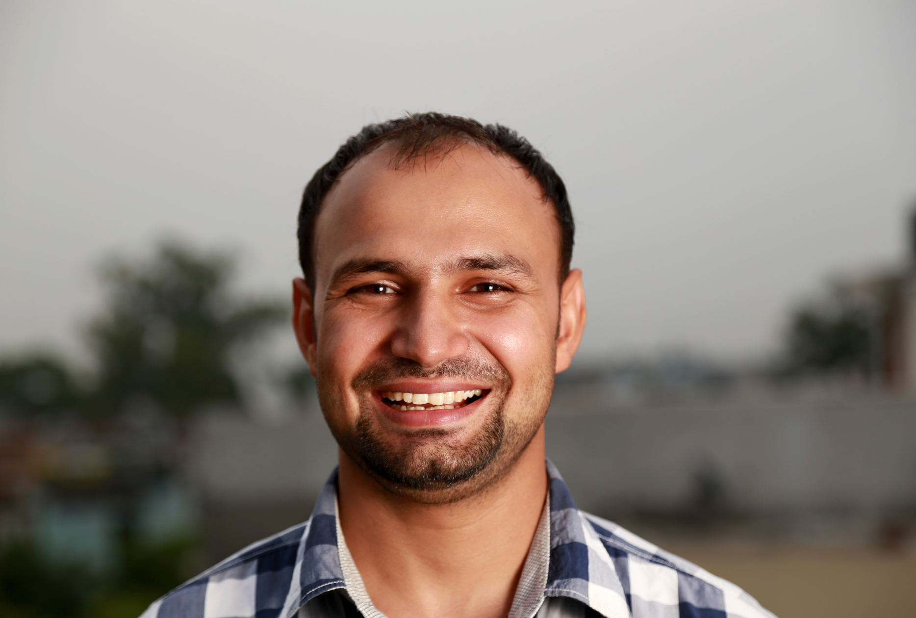 A man with a beard is smiling for the camera while wearing a plaid shirt.
