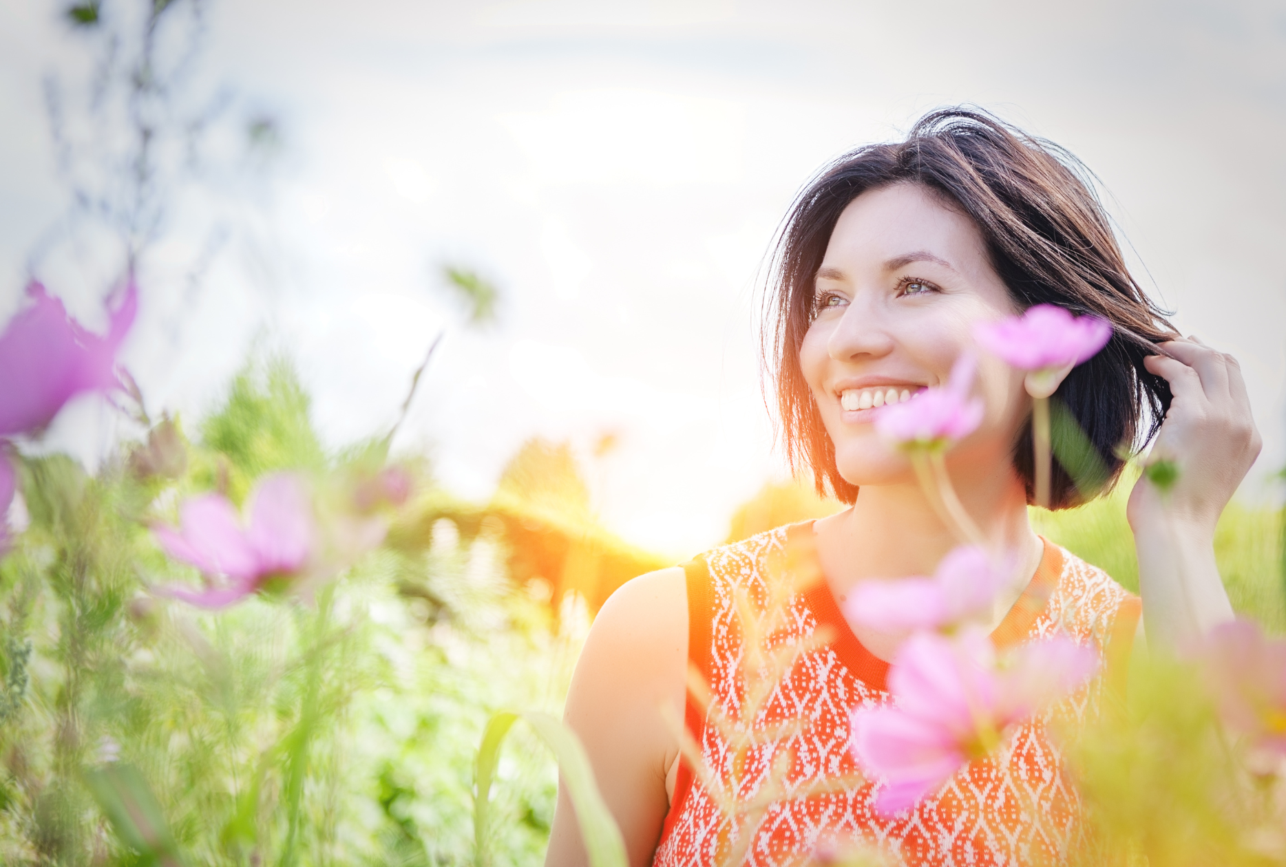 A woman is standing in a field of flowers and smiling.