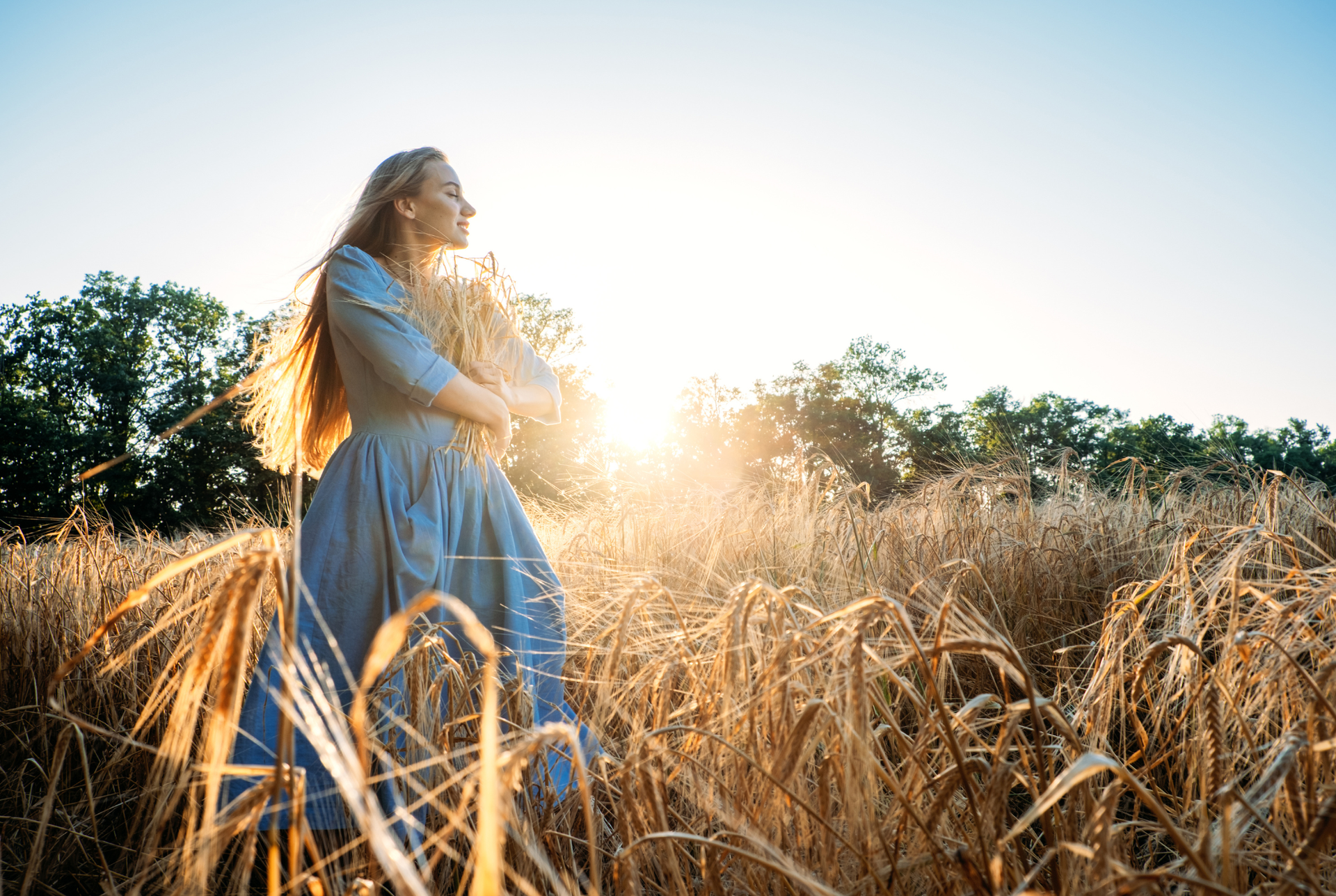 A woman in a blue dress is standing in a field of wheat.