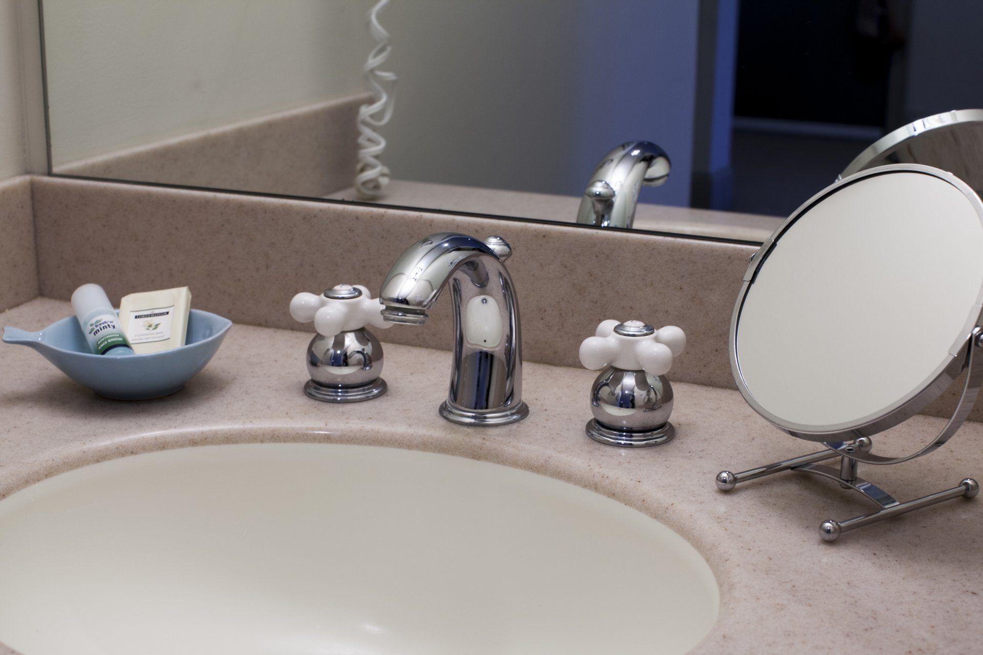 Close up of sink with white knobs, soap and a makeup mirror.