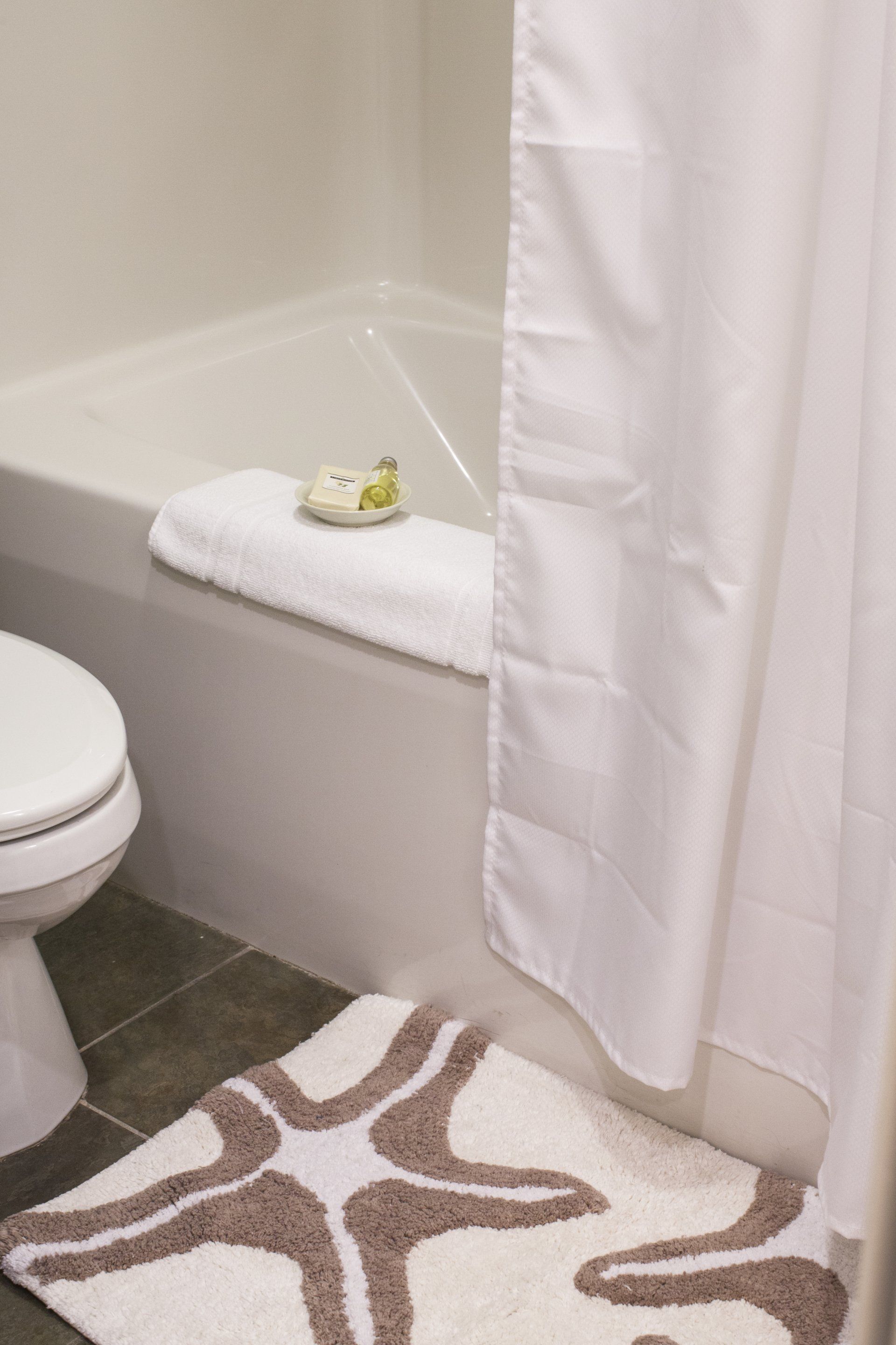 Bathroom with white shower curtain pulled back, towel on the edge of the tub and a rug in front of the tub with brown starfish on it.