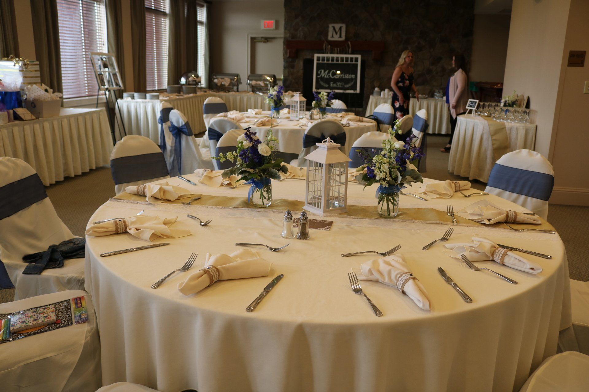 Banquet tables set with large candle centerpieces, glassware and silverware with white table cloths.