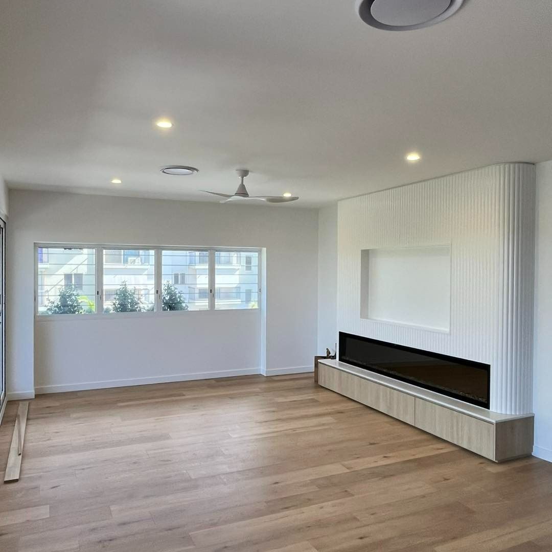 An Empty Living Room With Hardwood Floors and a Fireplace — JIC Projects Pty Ltd in Runaway Bay, QLD