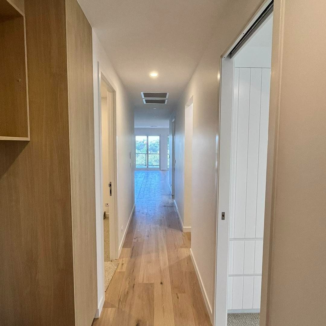A Long Hallway in a House With Wooden Floors and White Walls — JIC Projects Pty Ltd in Runaway Bay, QLD