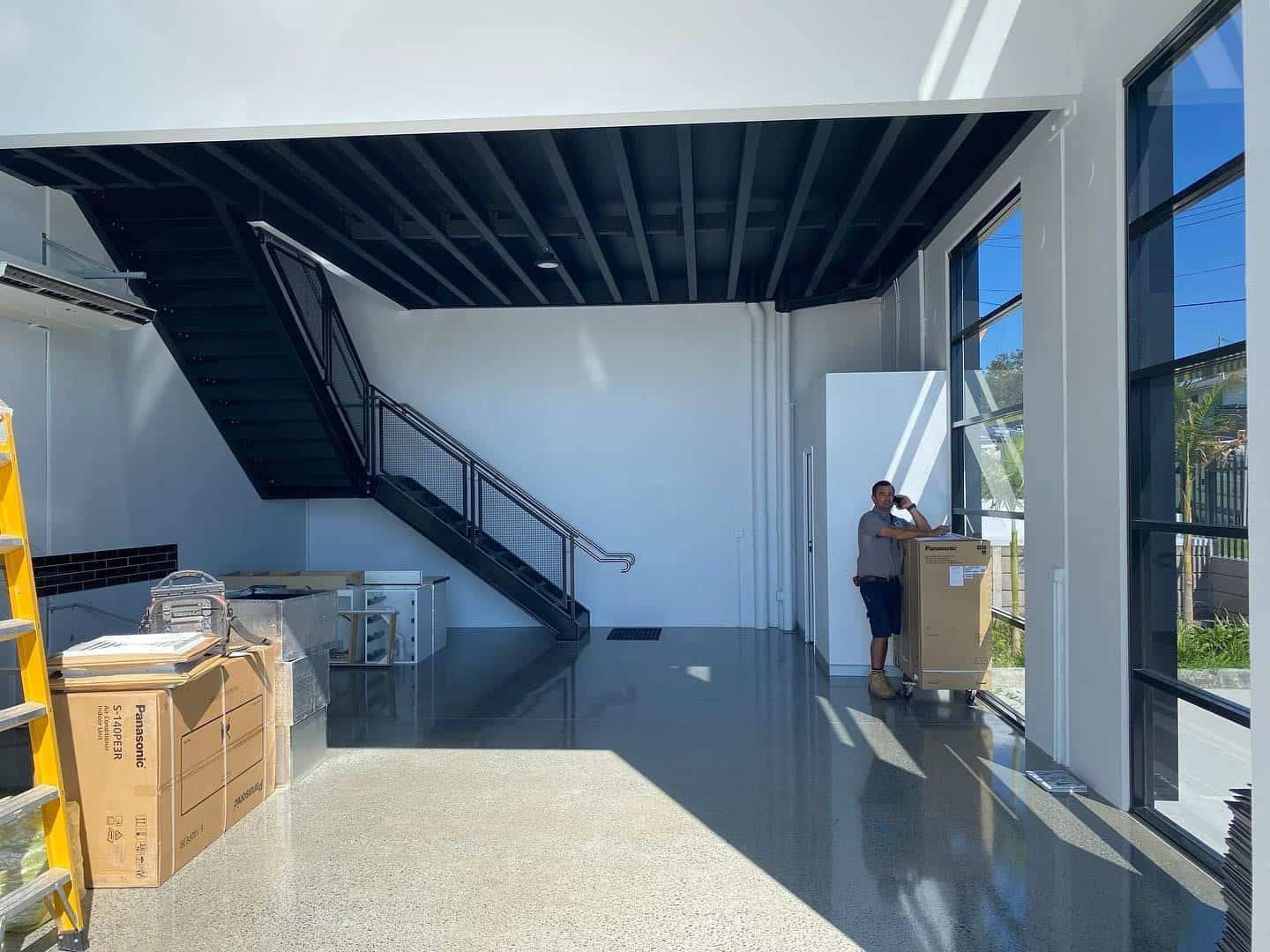 A Man is Carrying a Box in a Large Room With Stairs — JIC Projects Pty Ltd in Runaway Bay, QLD
