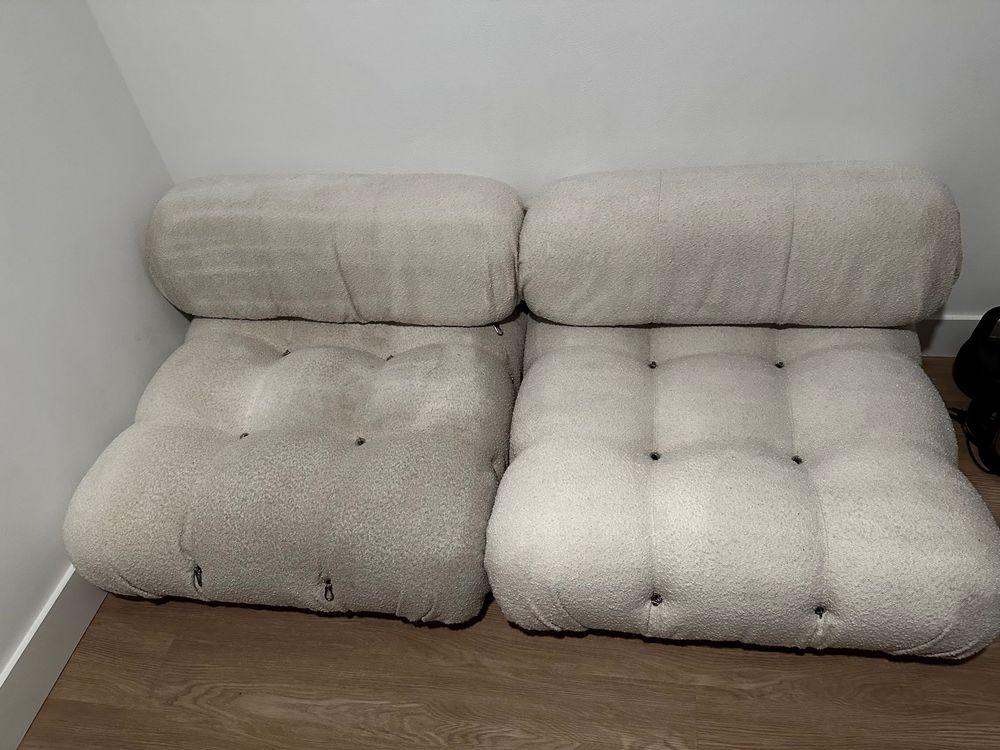 Two modular, low-profile white boucle fabric sofa sections with a tufted, grid-like pattern against a white wall.