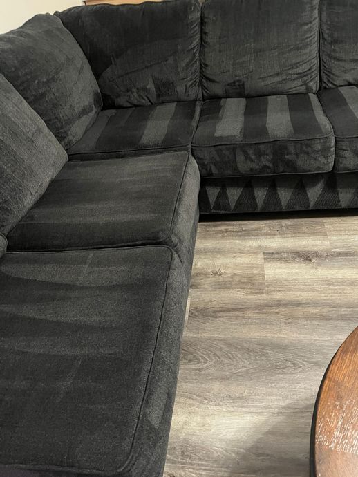 A charcoal gray sectional sofa sits on light wood-grain flooring, partially seen next to a circular wooden table.