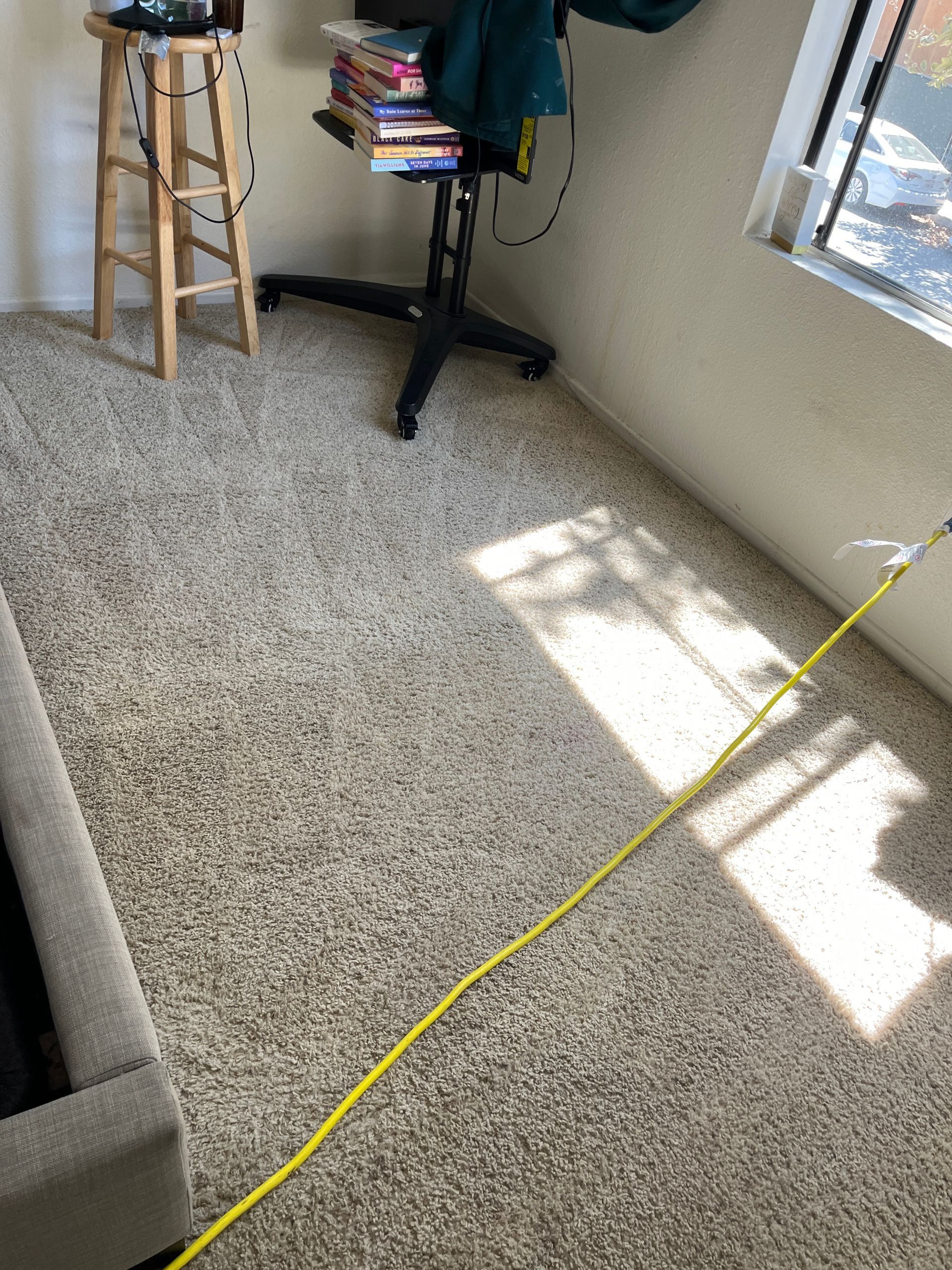A bright yellow power cord stretches across a carpeted room, leading toward a wooden stool and a desk chair.