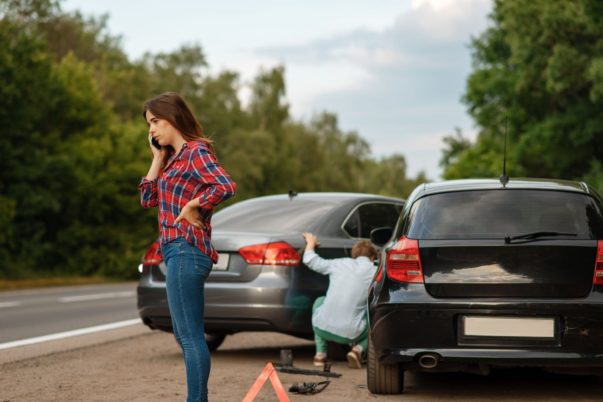 Woman on the phone after an auto accident while a man checks the damage