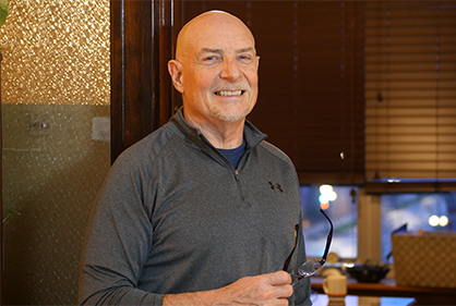 A bald man is smiling while holding a pair of glasses.