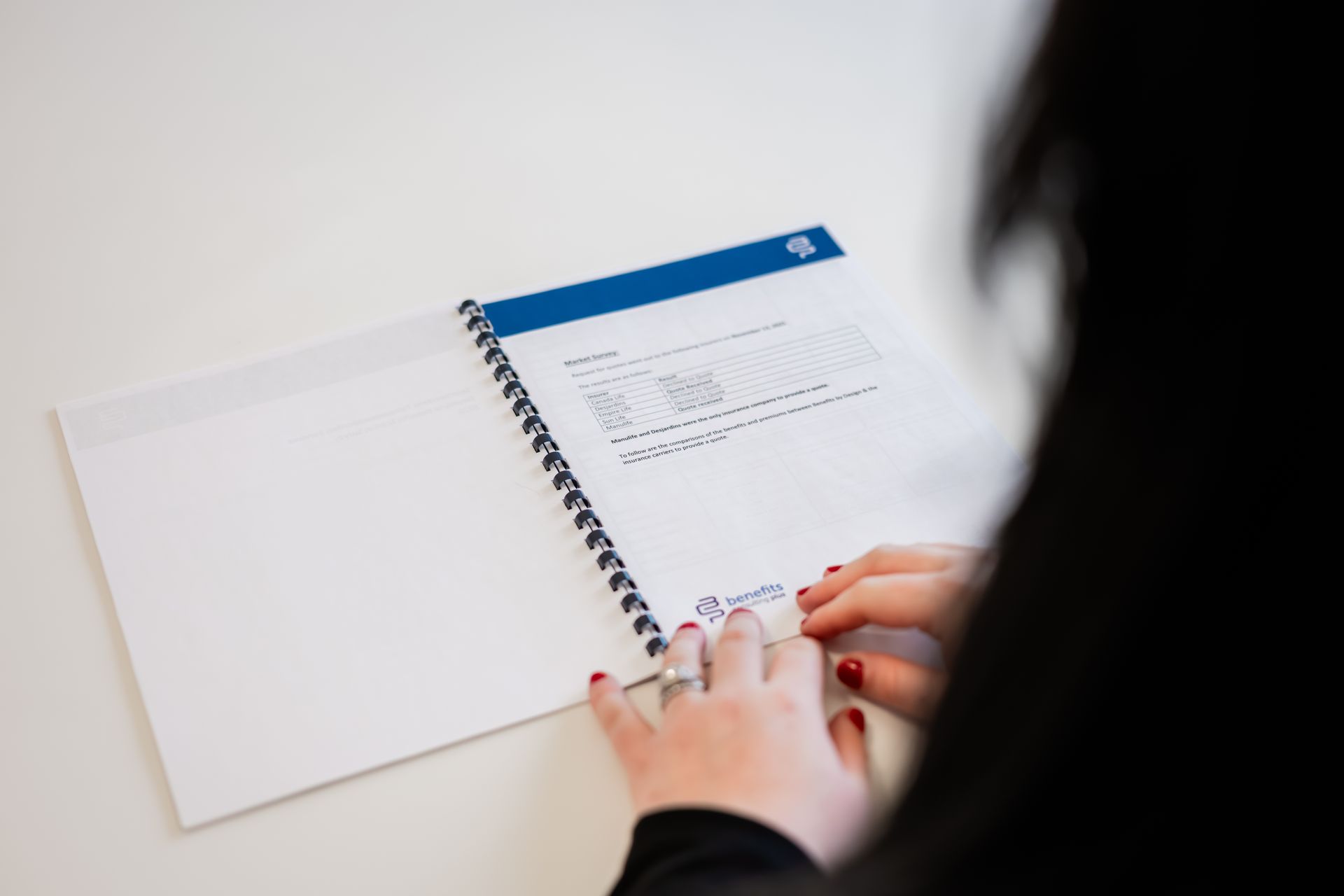 Person holding open spiral-bound notebook with printed text on a white table.