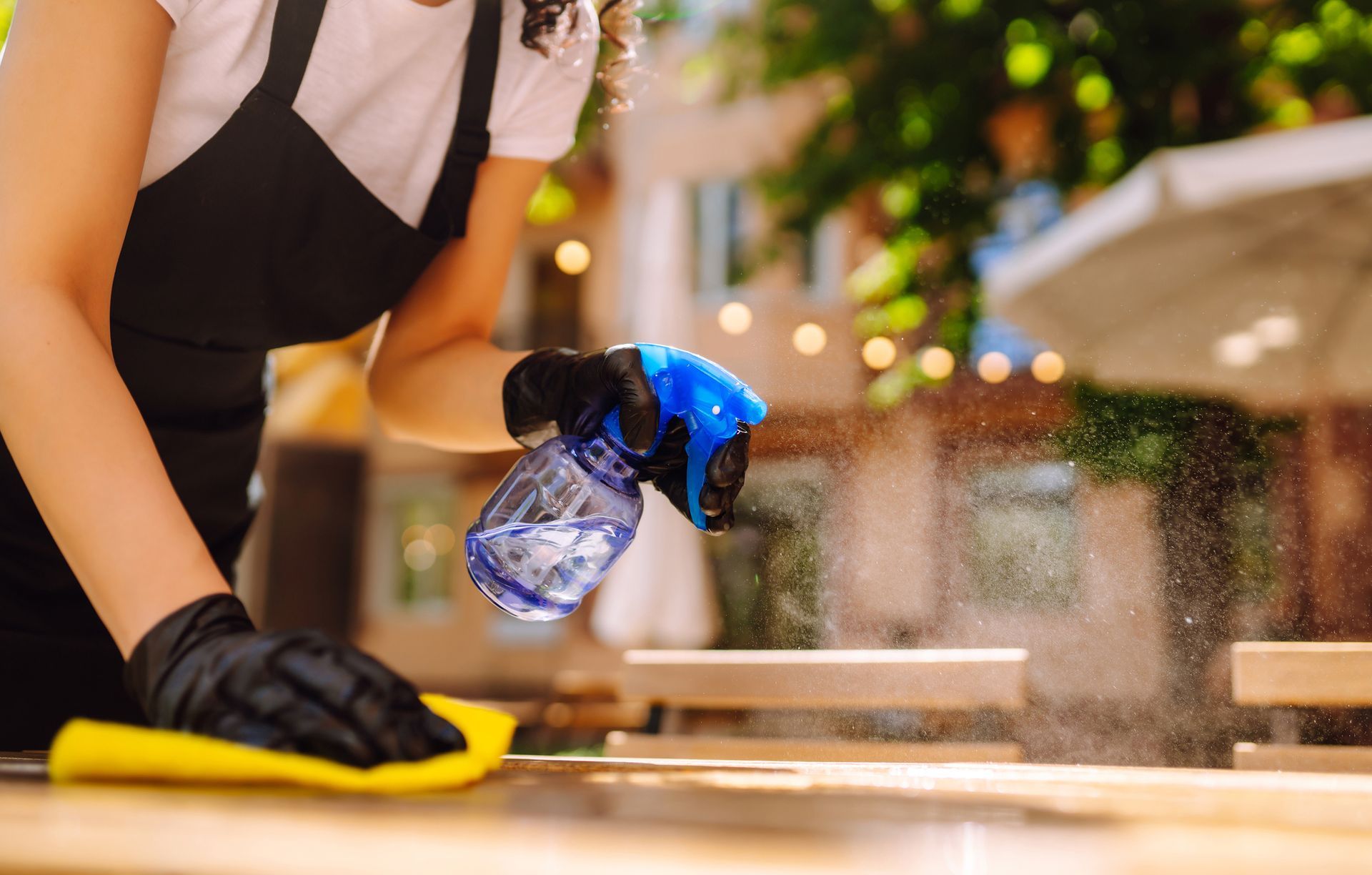 A woman is cleaning a table with a spray bottle and a cloth.