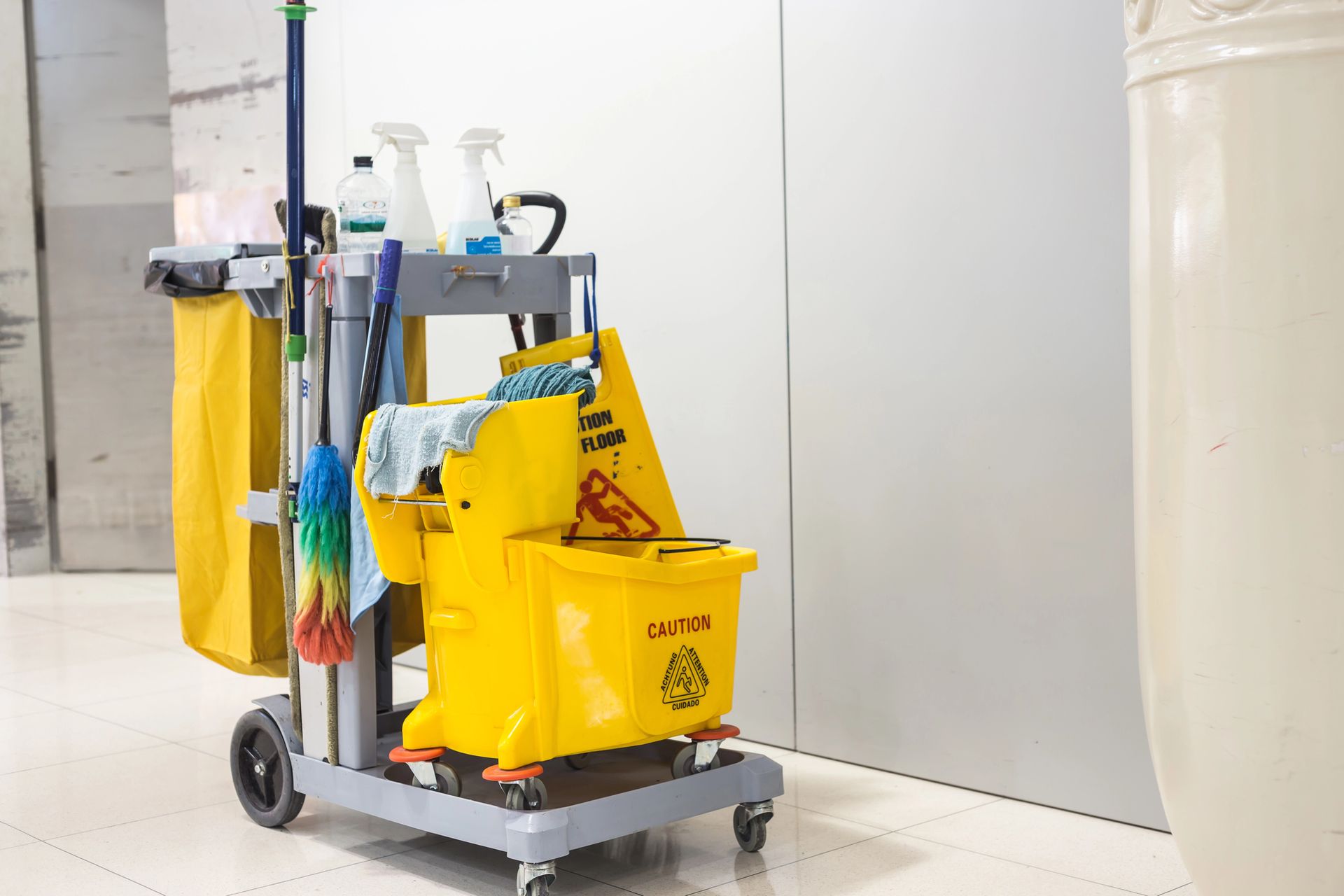 Janitor cart with yellow cleaning bags and supplies beside a white wall in a hallway