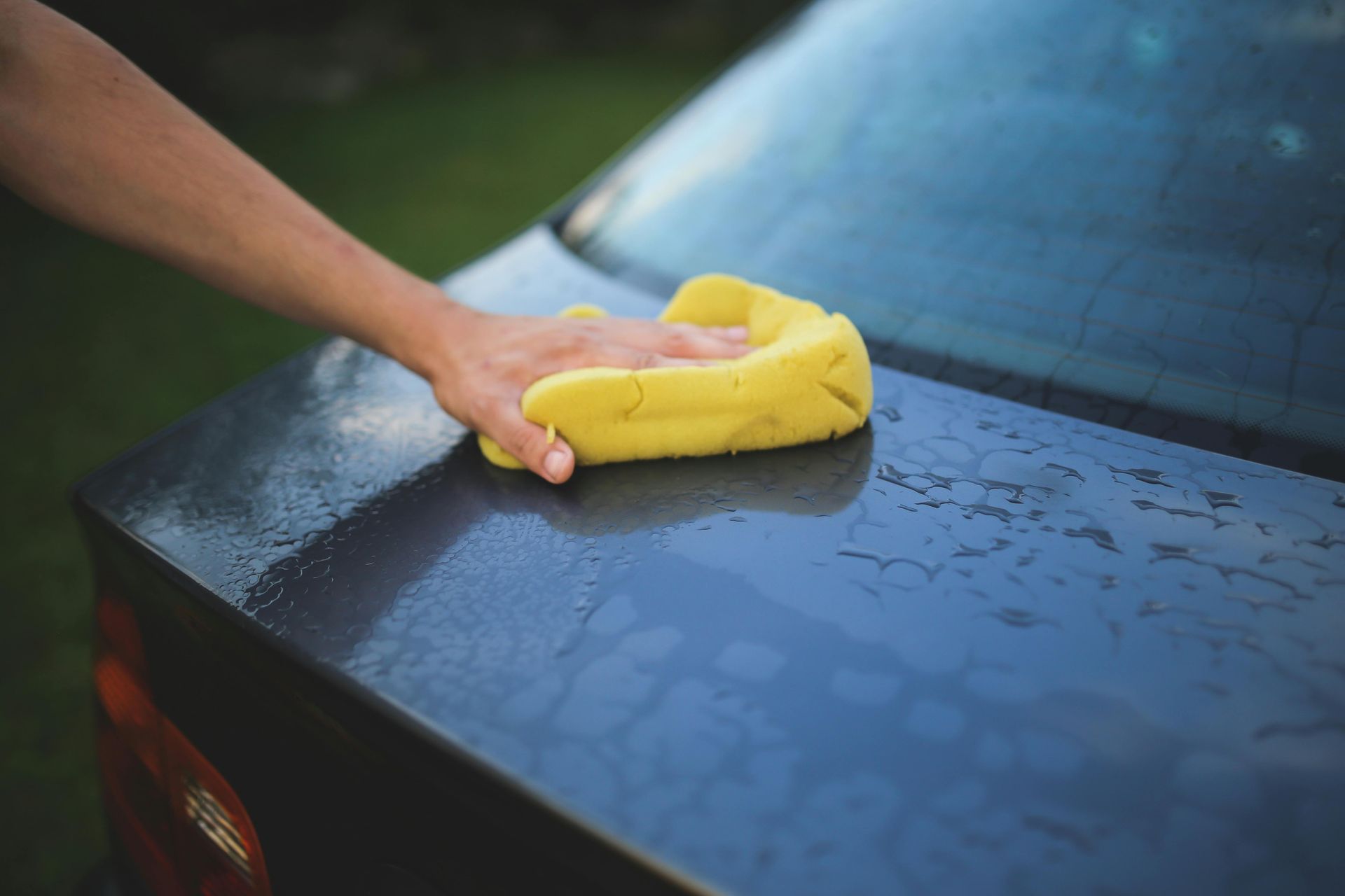 A person is cleaning a car with a yellow sponge.