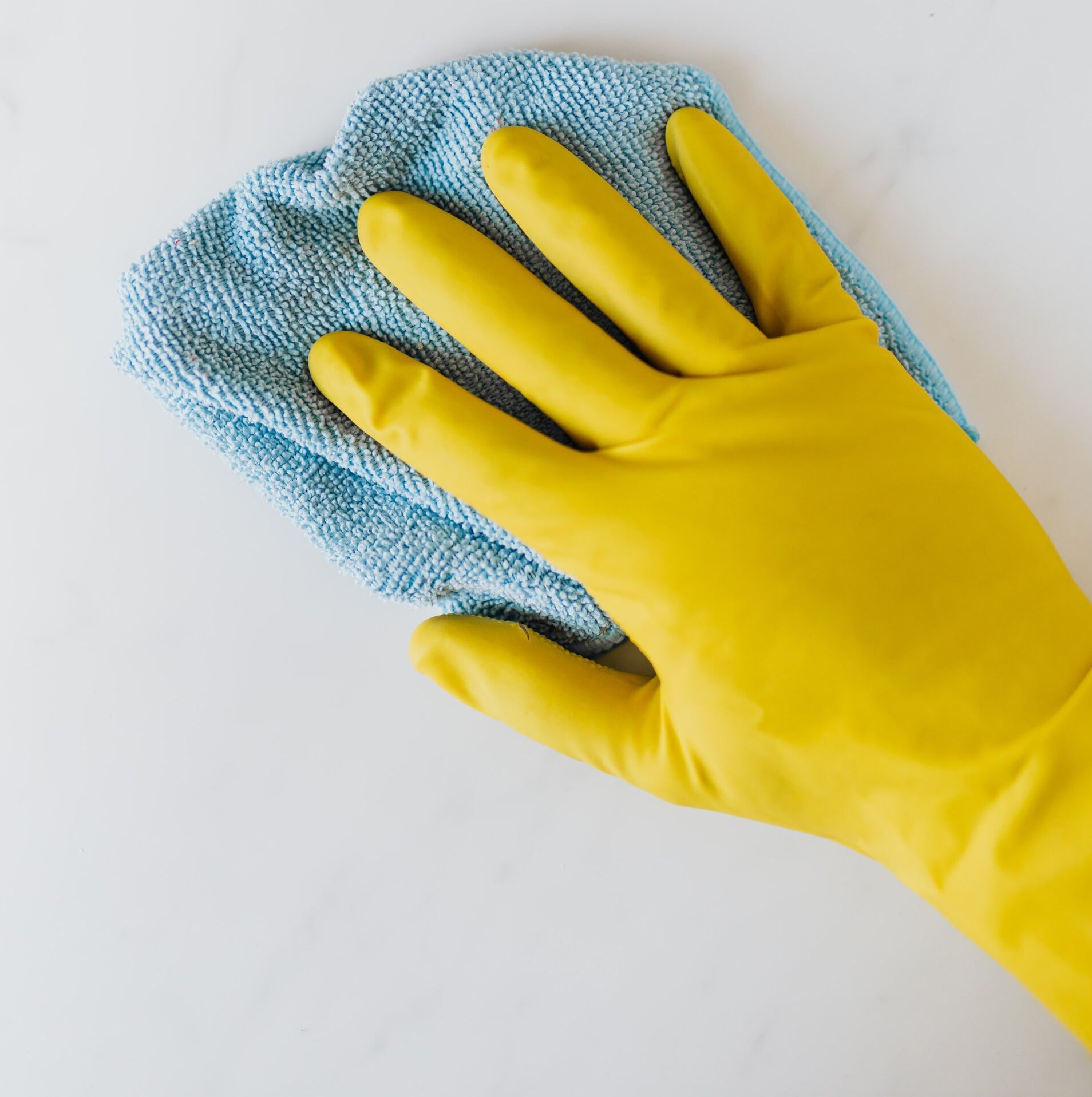 A person wearing a yellow rubber glove is cleaning a white surface with a blue cloth.