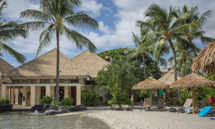 A beach with thatched umbrellas and a house in the background