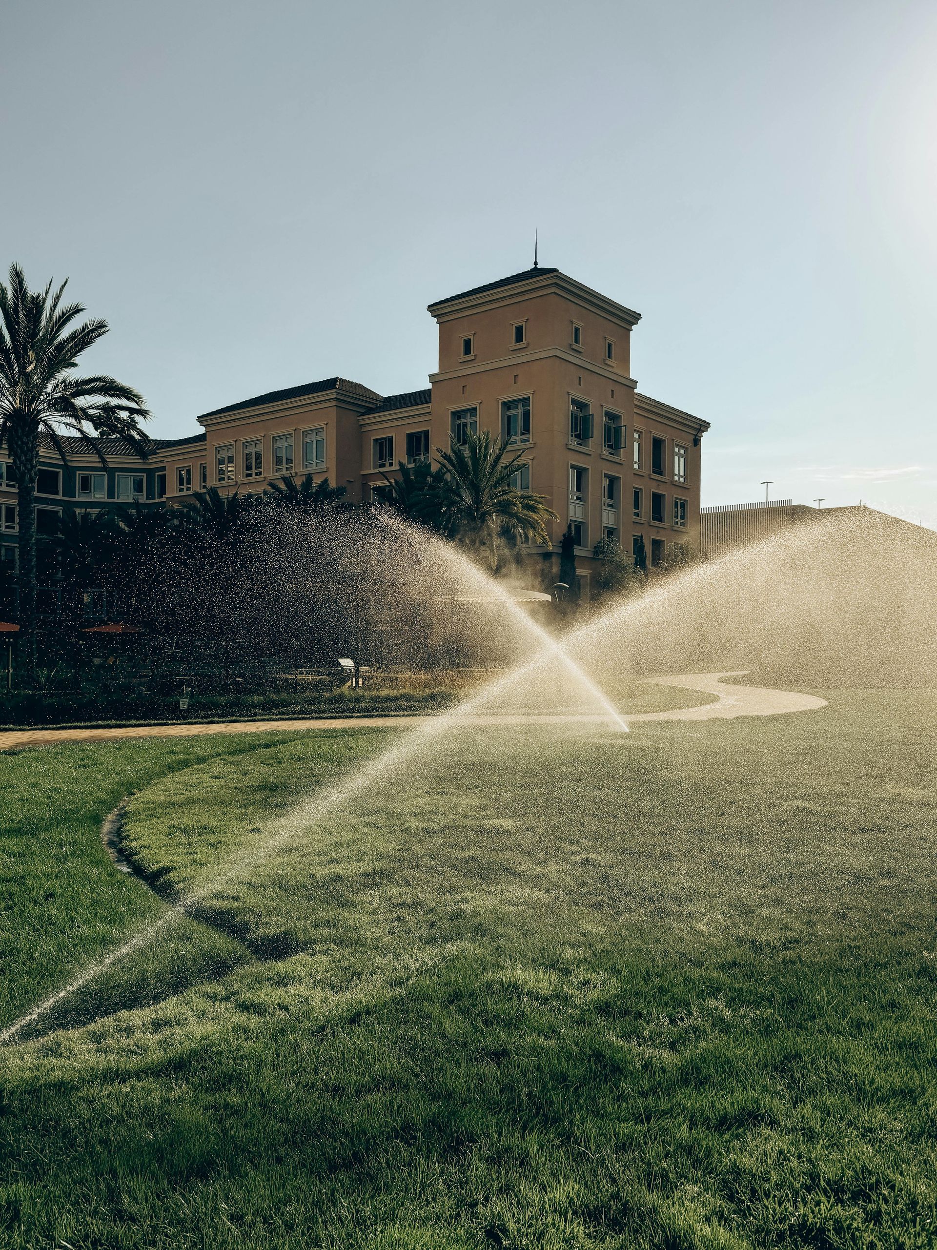 A sprinkler is spraying water on a lush green field in front of a large building.