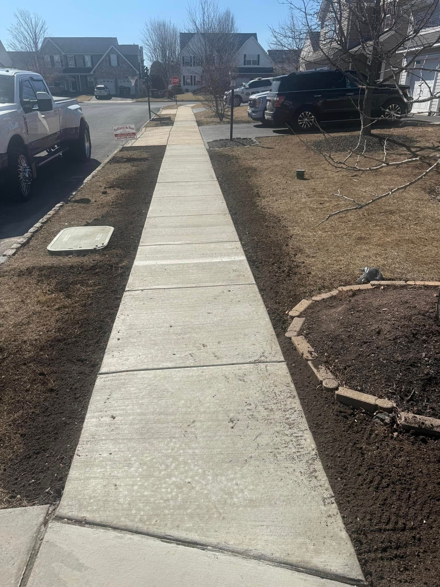 A sidewalk in a residential neighborhood with cars parked on the side of it.