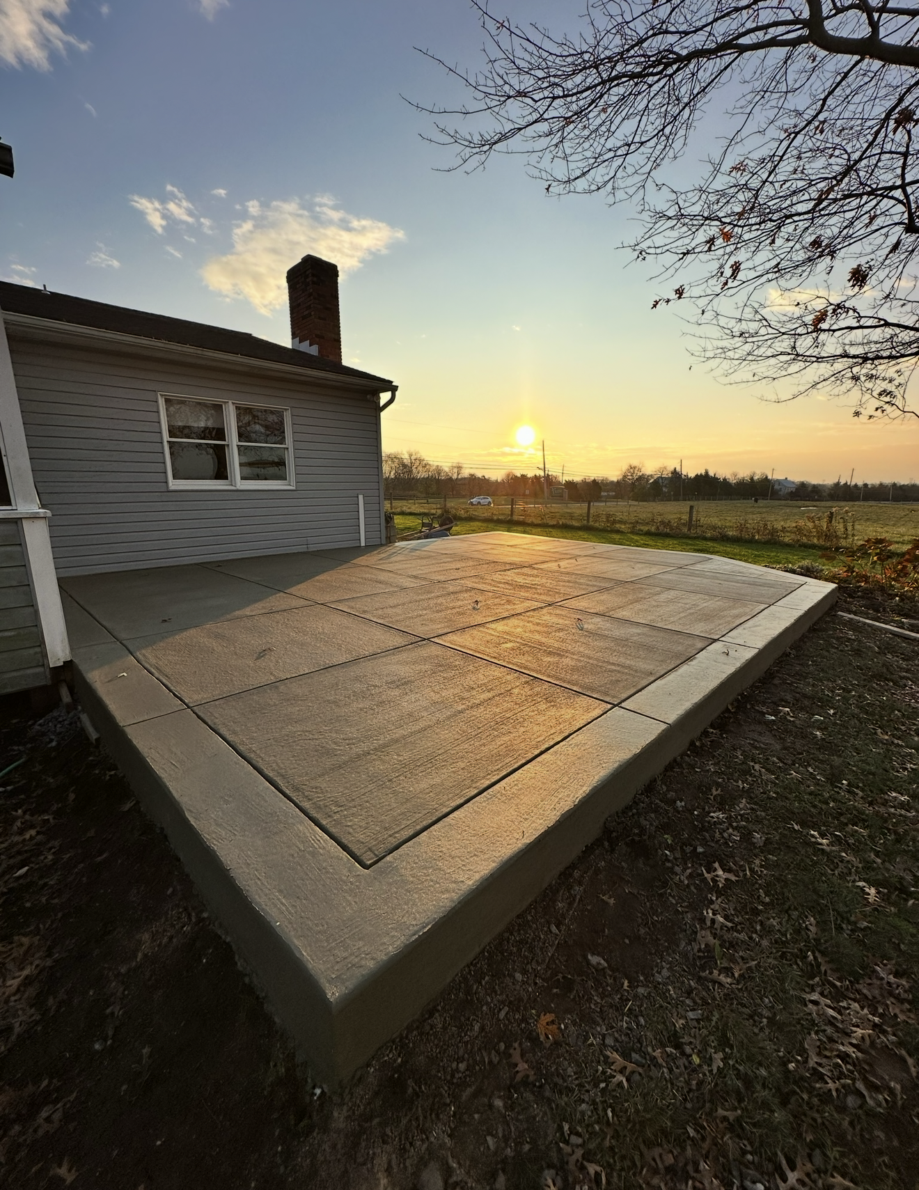 A concrete patio in front of a house with a sunset in the background.