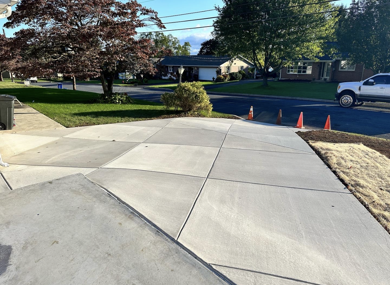 A white truck is parked on the side of the road next to a concrete driveway.