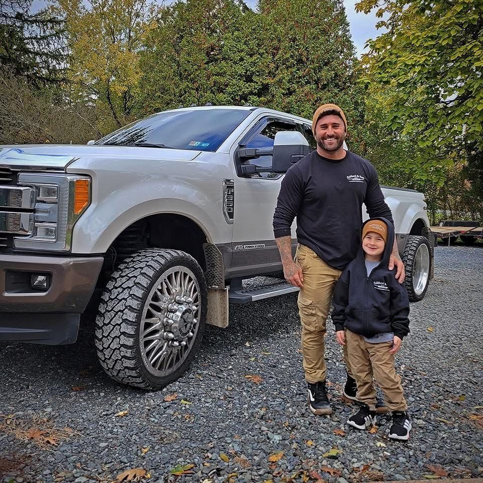 A man and a boy are standing in front of a truck.