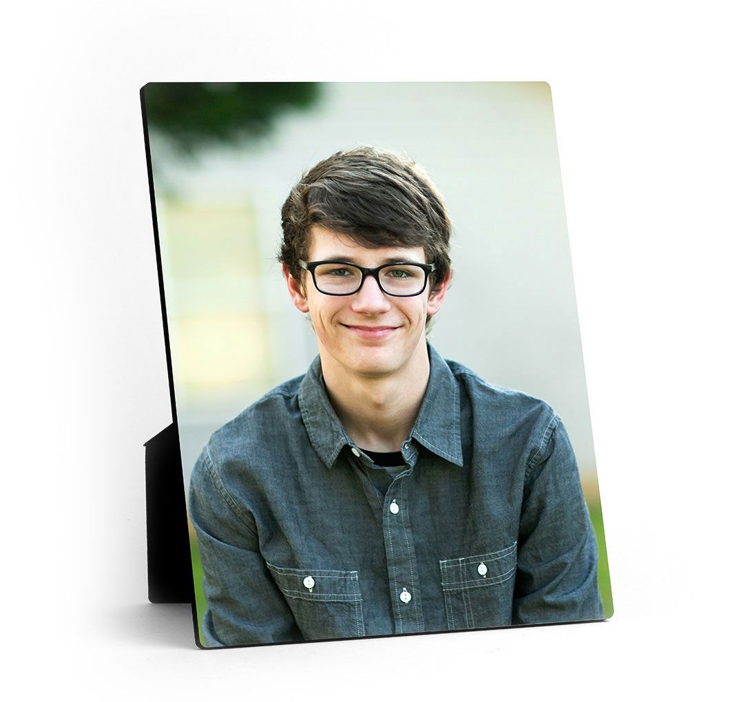 An easel print displaying a picture of a man and woman standing next to each other outdoors rests on top of a desk next to a small plant.