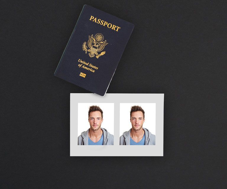 A passport is sitting on top of a map of the world along with other objects like a camera, camera lens and a stack of small polaroids.