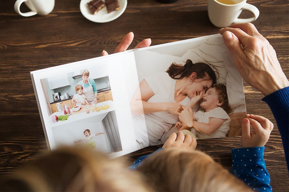 A person is holding a photo album with pictures of a child with their mother and grandmother