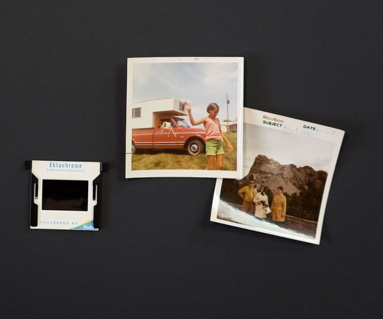 A person is holding a black and white photo of a bride and groom over a wooden table, with other black and white wedding photos placed around the table. 