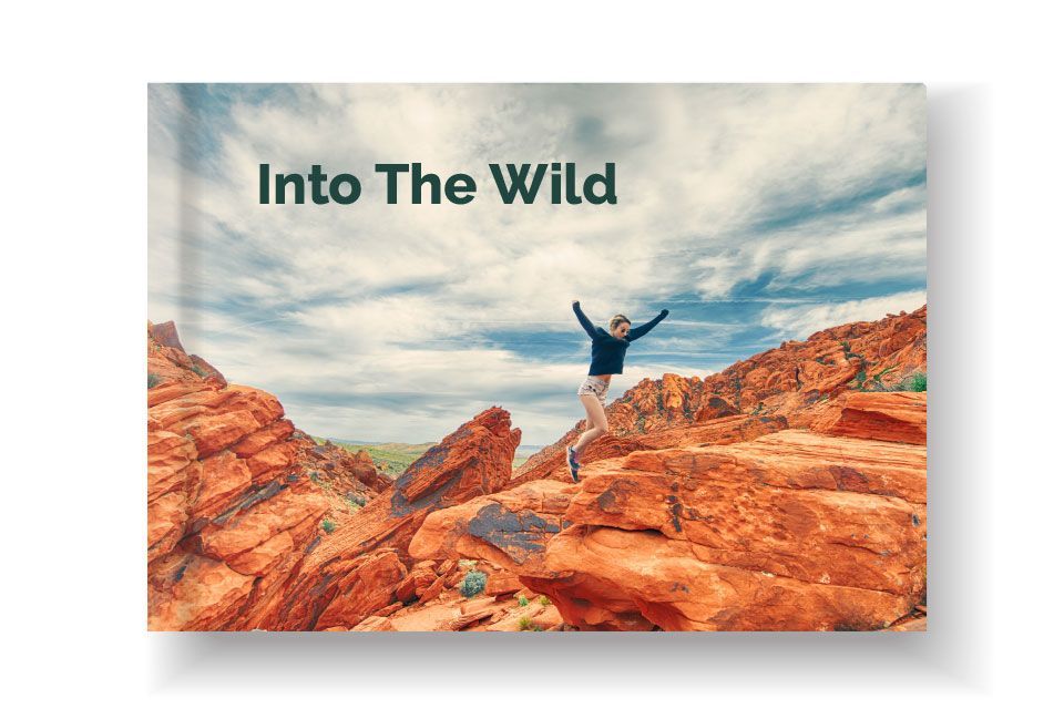An image wrapped photo album for a vacation. The book is called Into the Wild and features a young woman jumping off a rock formation.
