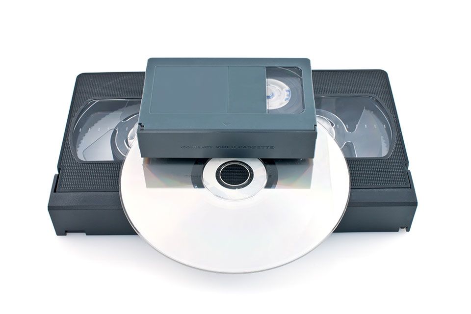 A VHS tape, video casette tape and DVD stacked together