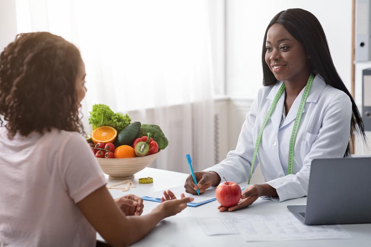 A woman is sitting at a table talking to a nutritionist who is holding an apple.