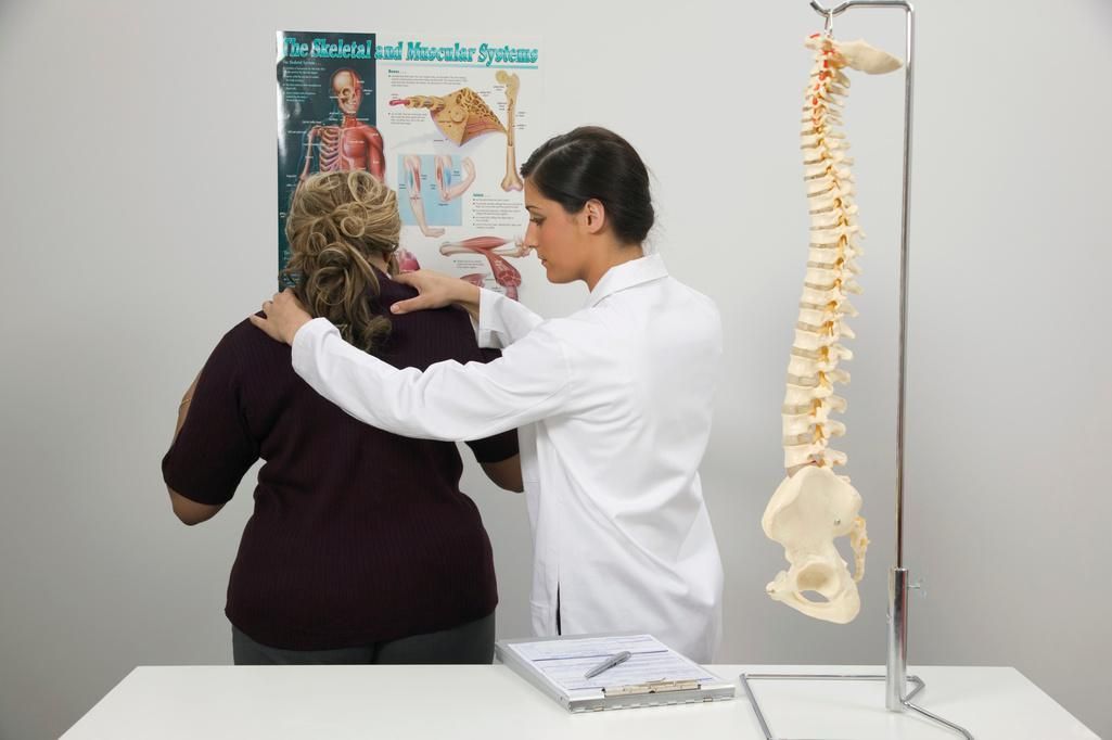 A doctor is examining a patient 's back in front of a spine model