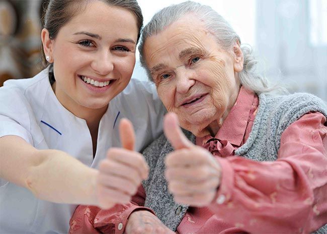 A nurse is giving an elderly woman a thumbs up.