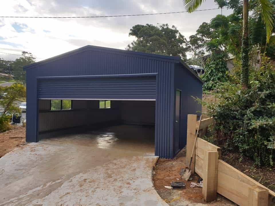 A Blue Garage With a Garage Door Open and a Driveway Leading to It — Hastings Valley Sheds in Wauchope, NSW