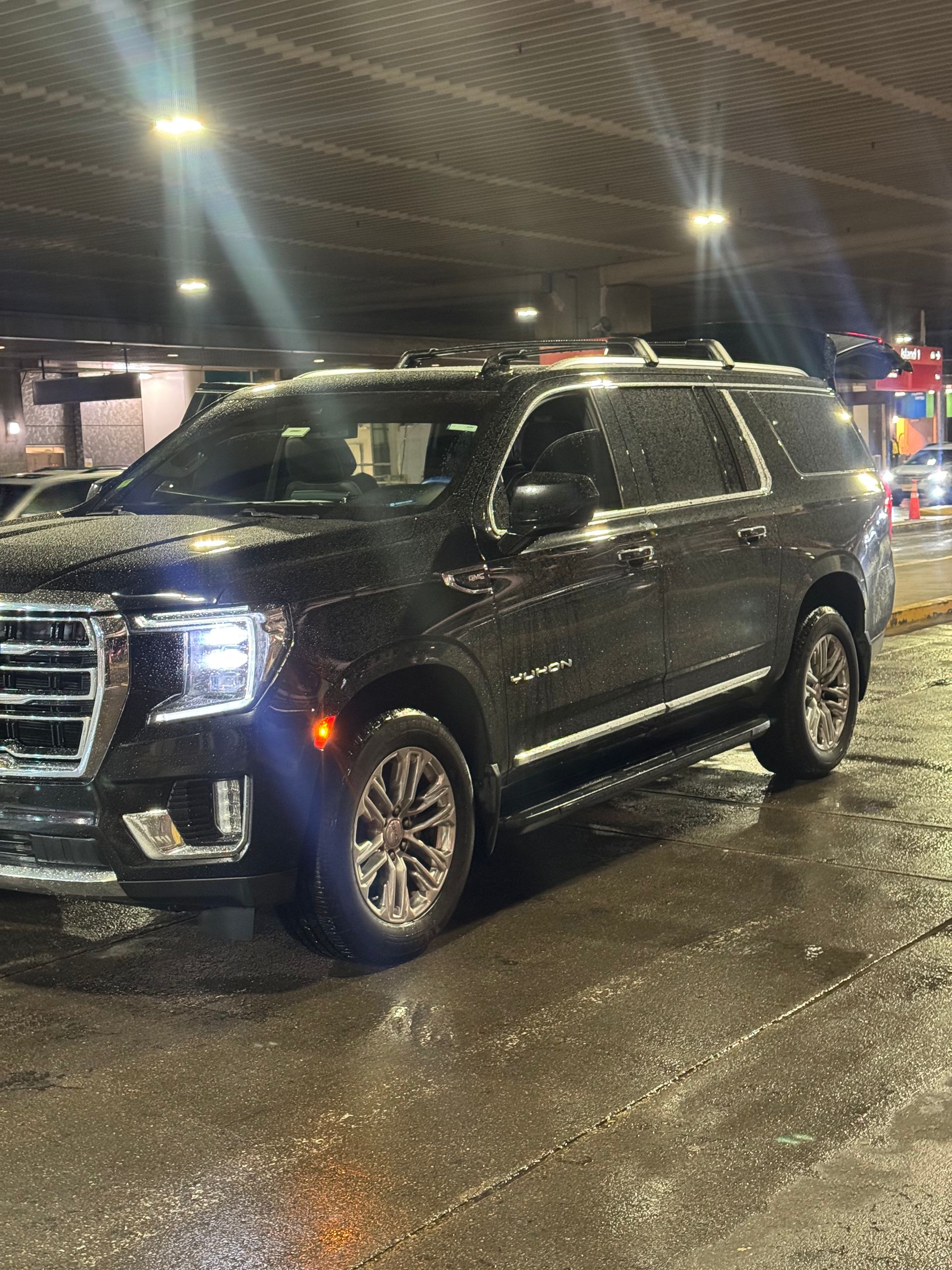 Black SUV parked at night in a wet parking lot under bright lights