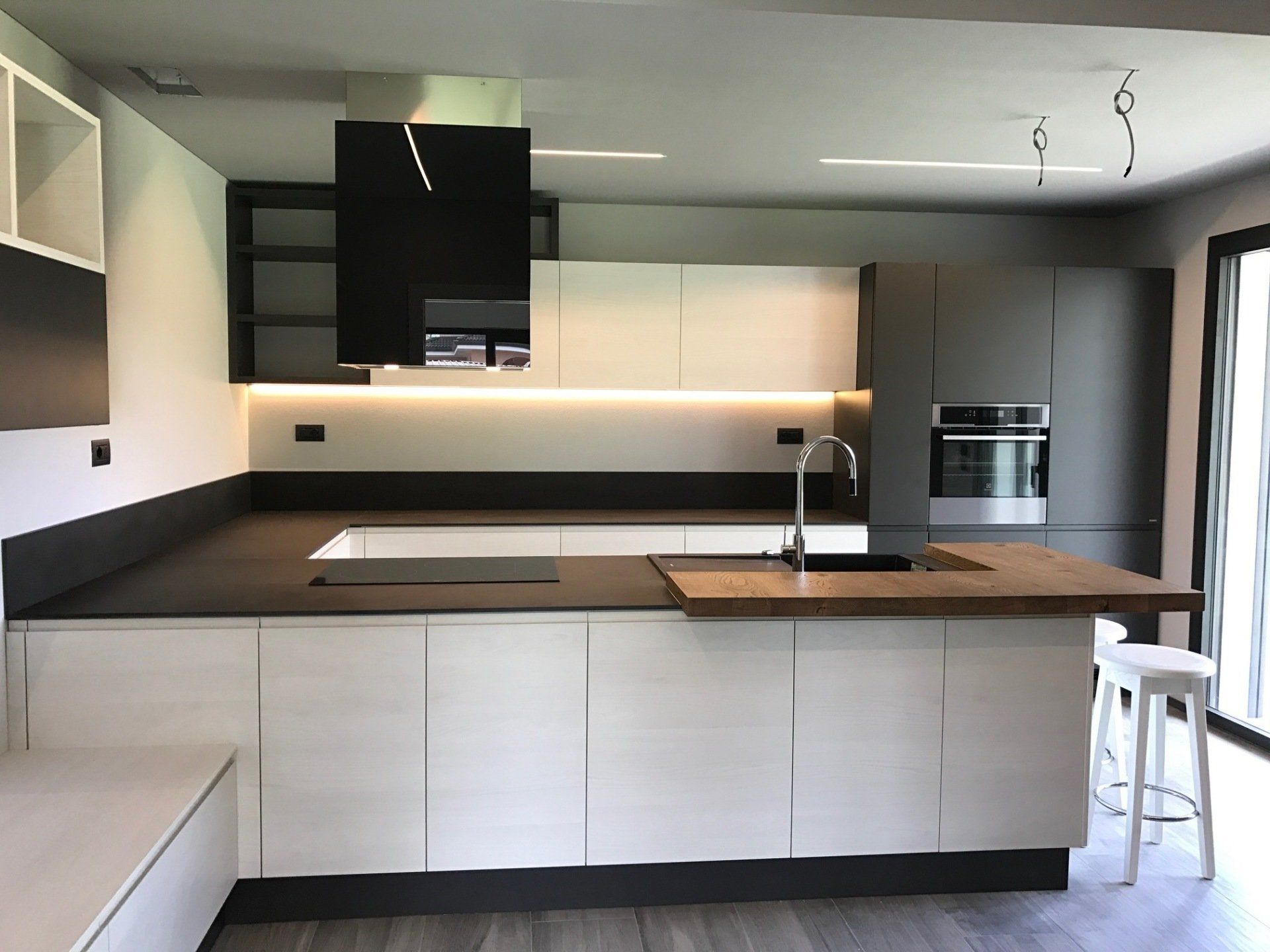 Cucina moderna con mobili in legno chiaro, ripiani scuri e cappa nera.